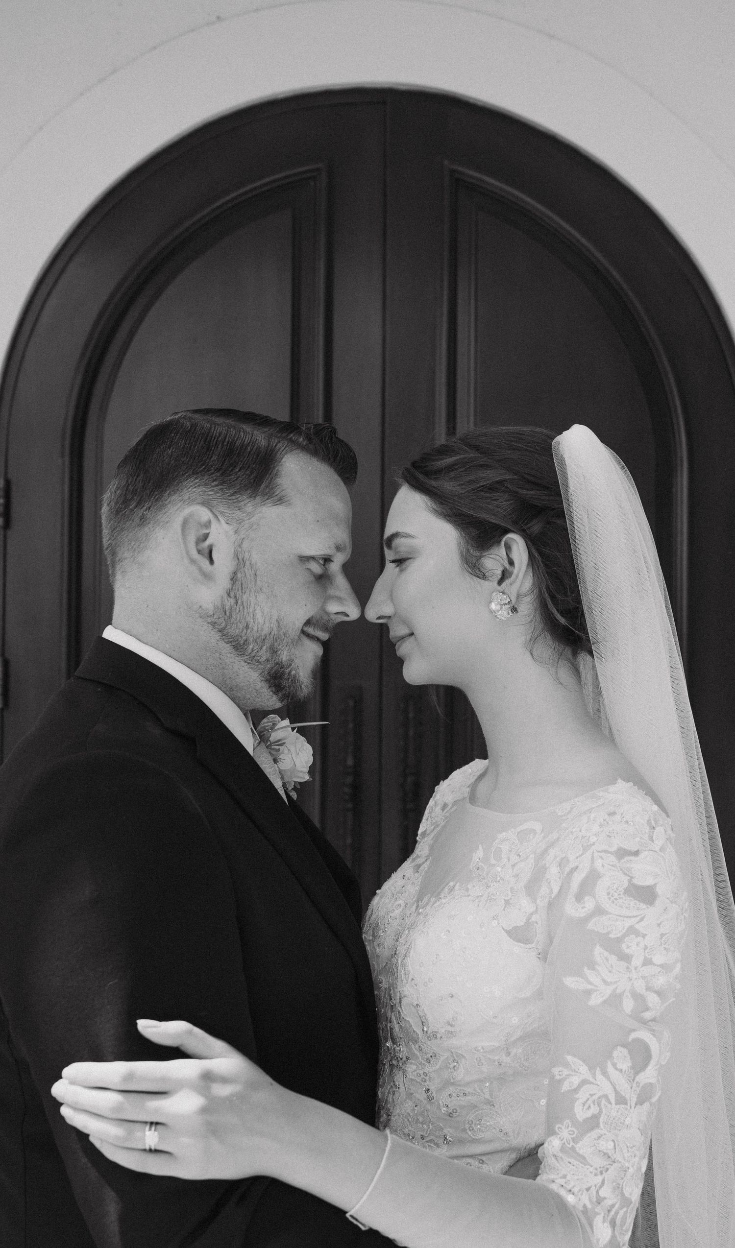 A romantic black and white wedding portrait showing a couple in formal attire sharing an intimate moment.