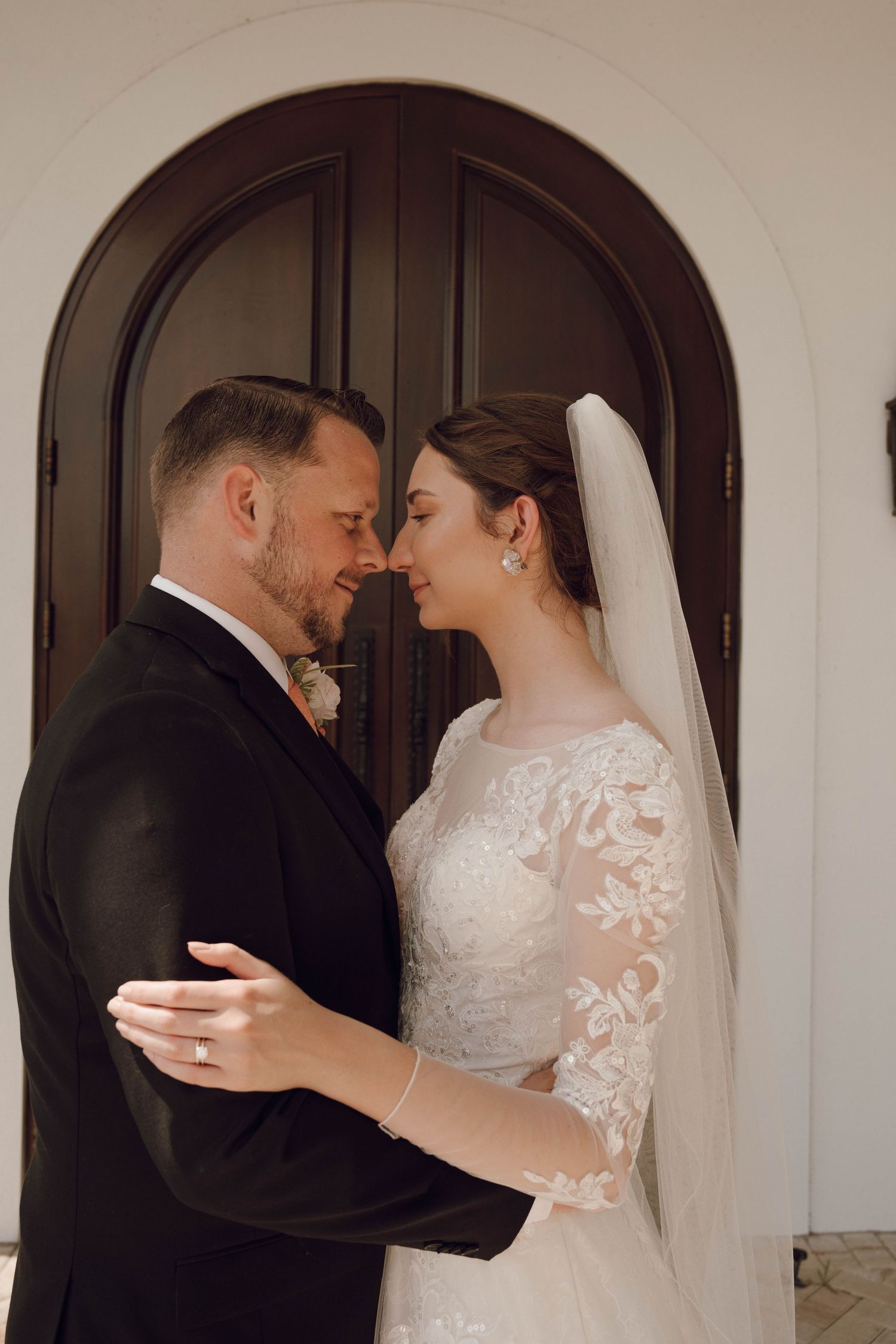 A tender wedding moment captured in front of an arched doorway with the couple in traditional attire.