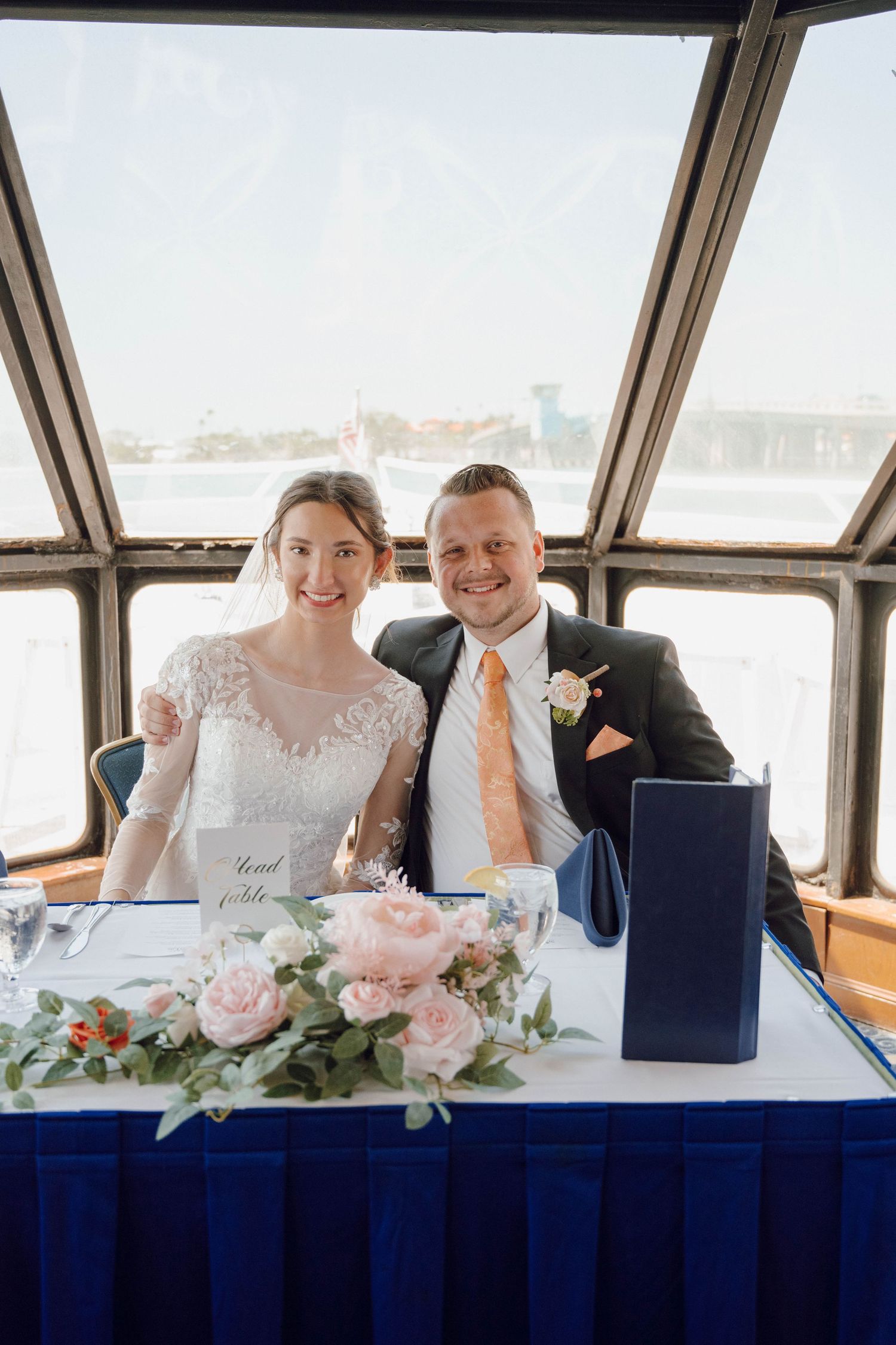 Wedding party seated at a table on a boat with panoramic windows overlooking the water.