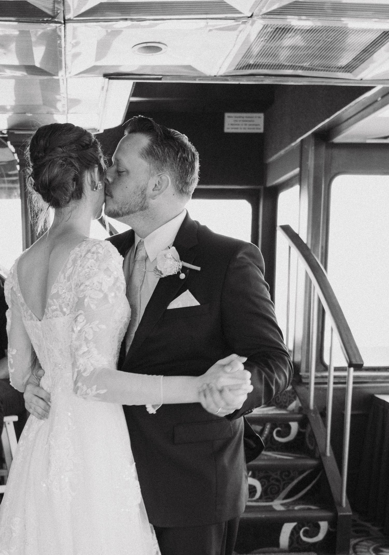 A black and white photo of a wedding couple sharing a dance in what appears to be a vintage train car.