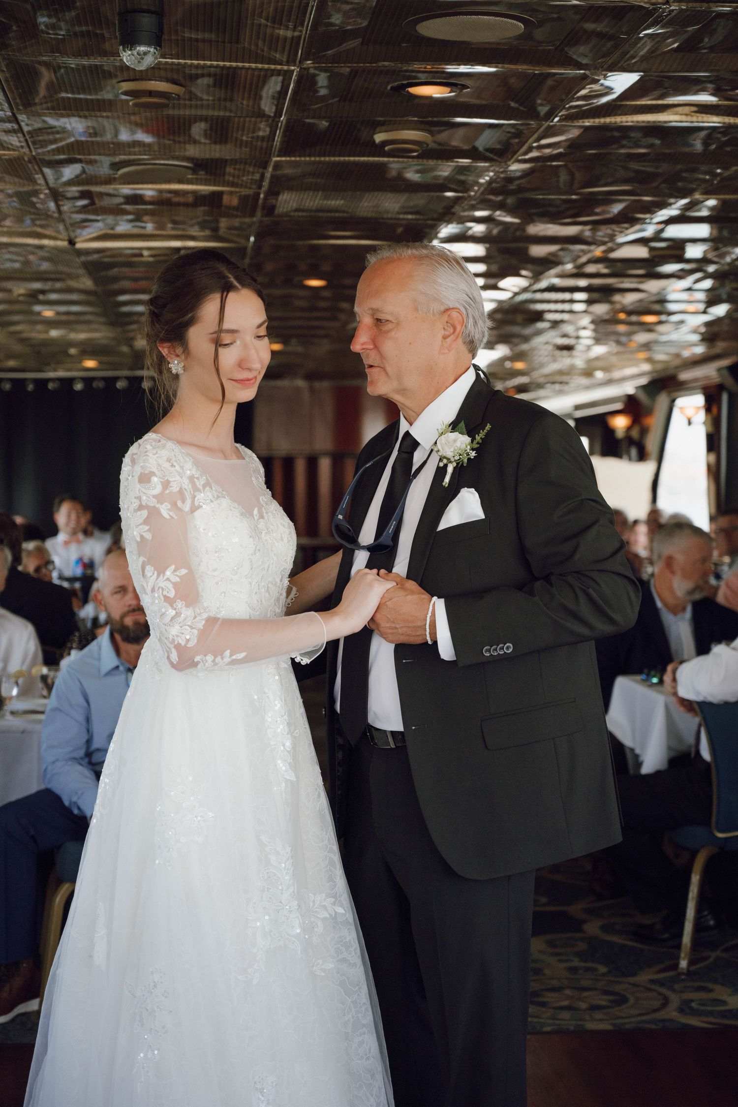 A couple shares a dance in formal attire under an ornate mirrored ceiling.