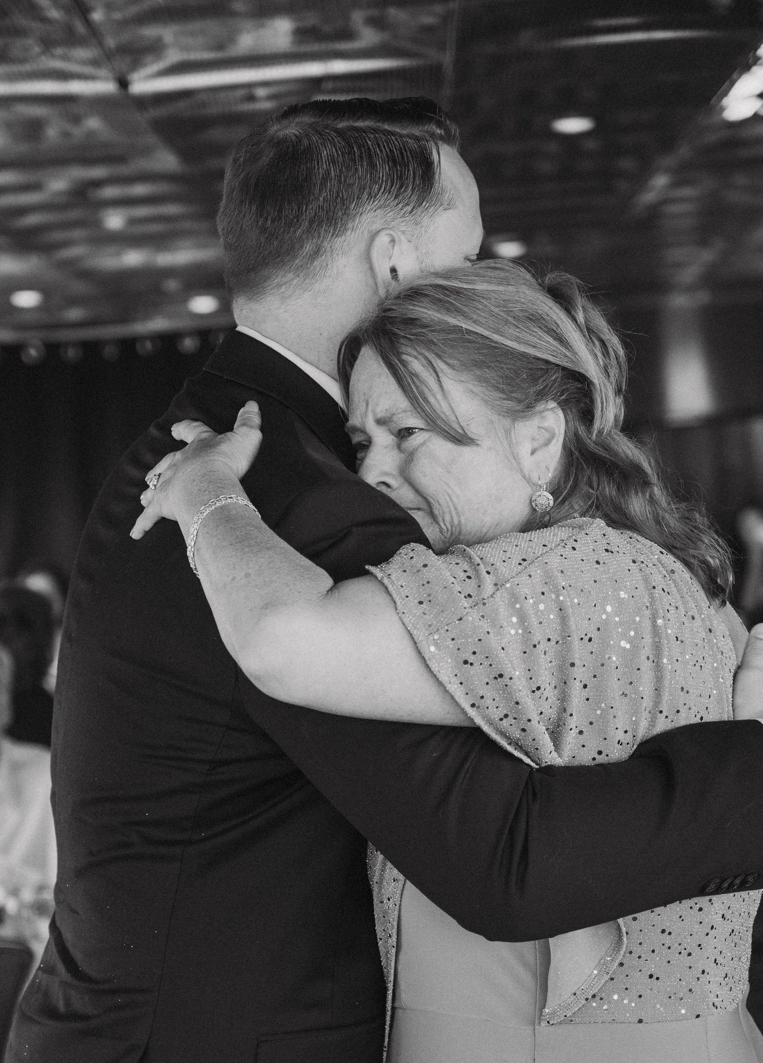 A black and white photograph of a couple sharing an emotional dance at a wedding reception.