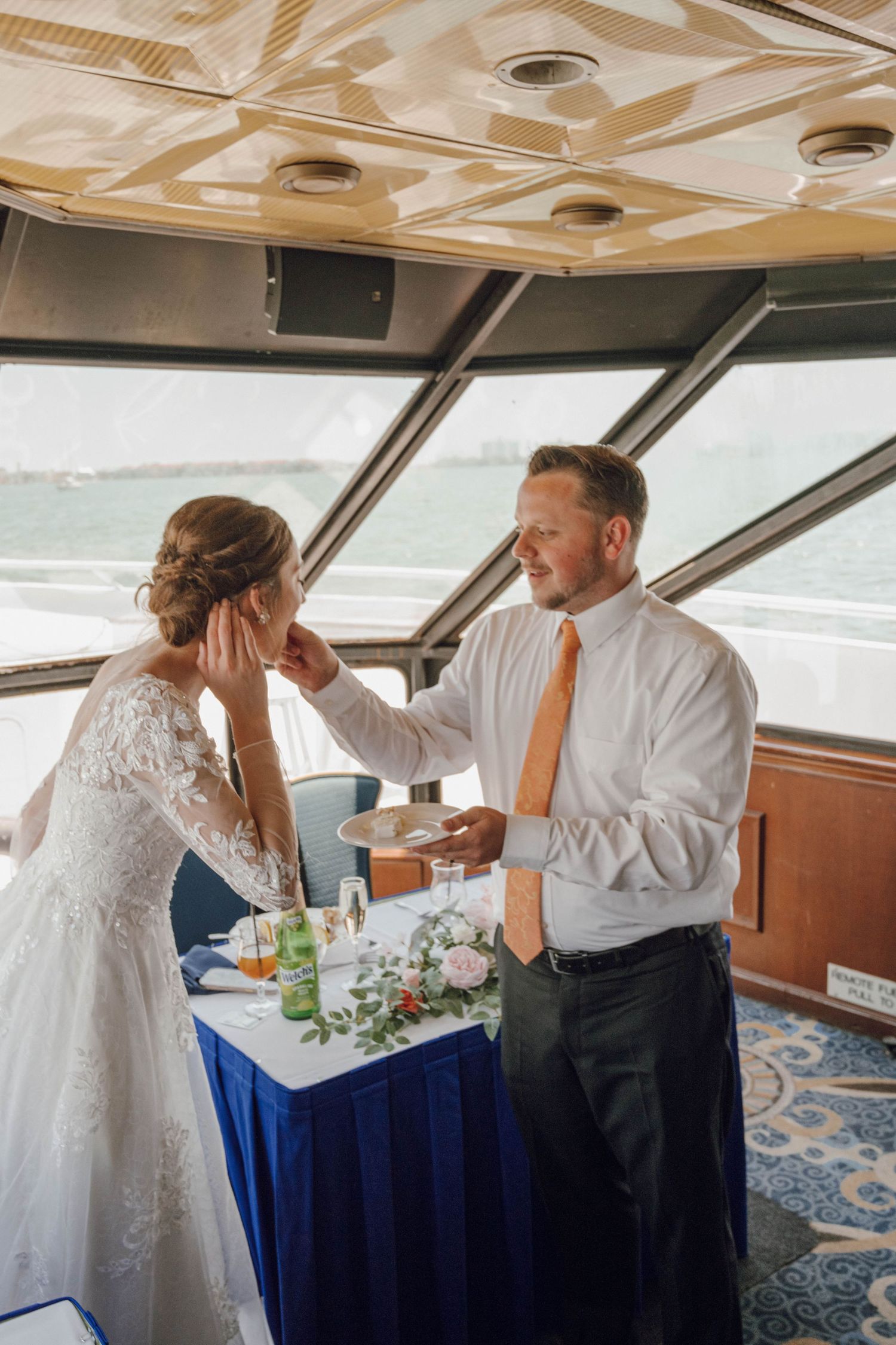 A tender moment between newlyweds sharing cake aboard a boat during their wedding reception celebration.