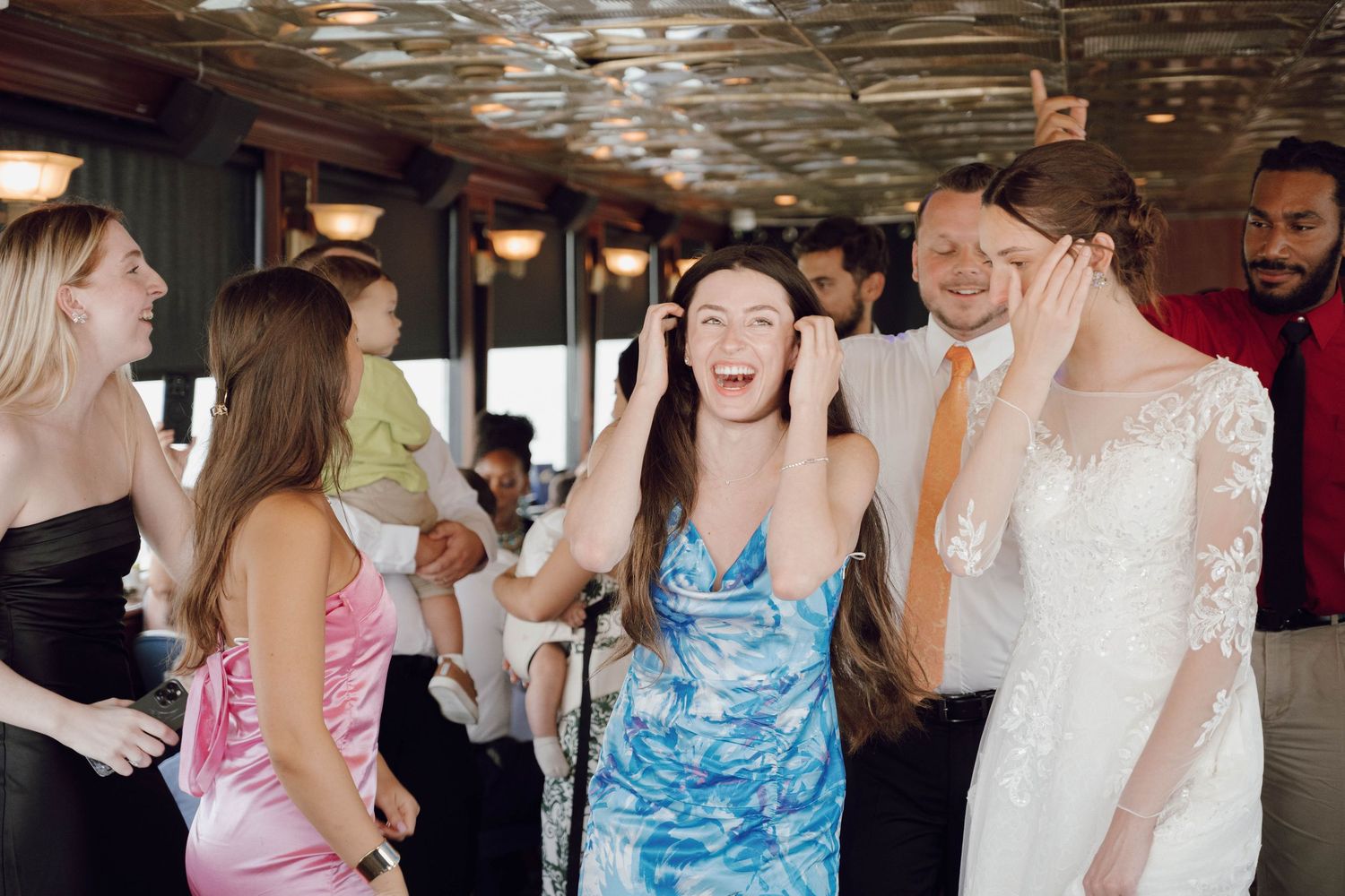Wedding guests dancing and celebrating at a reception venue with reflective ceiling.