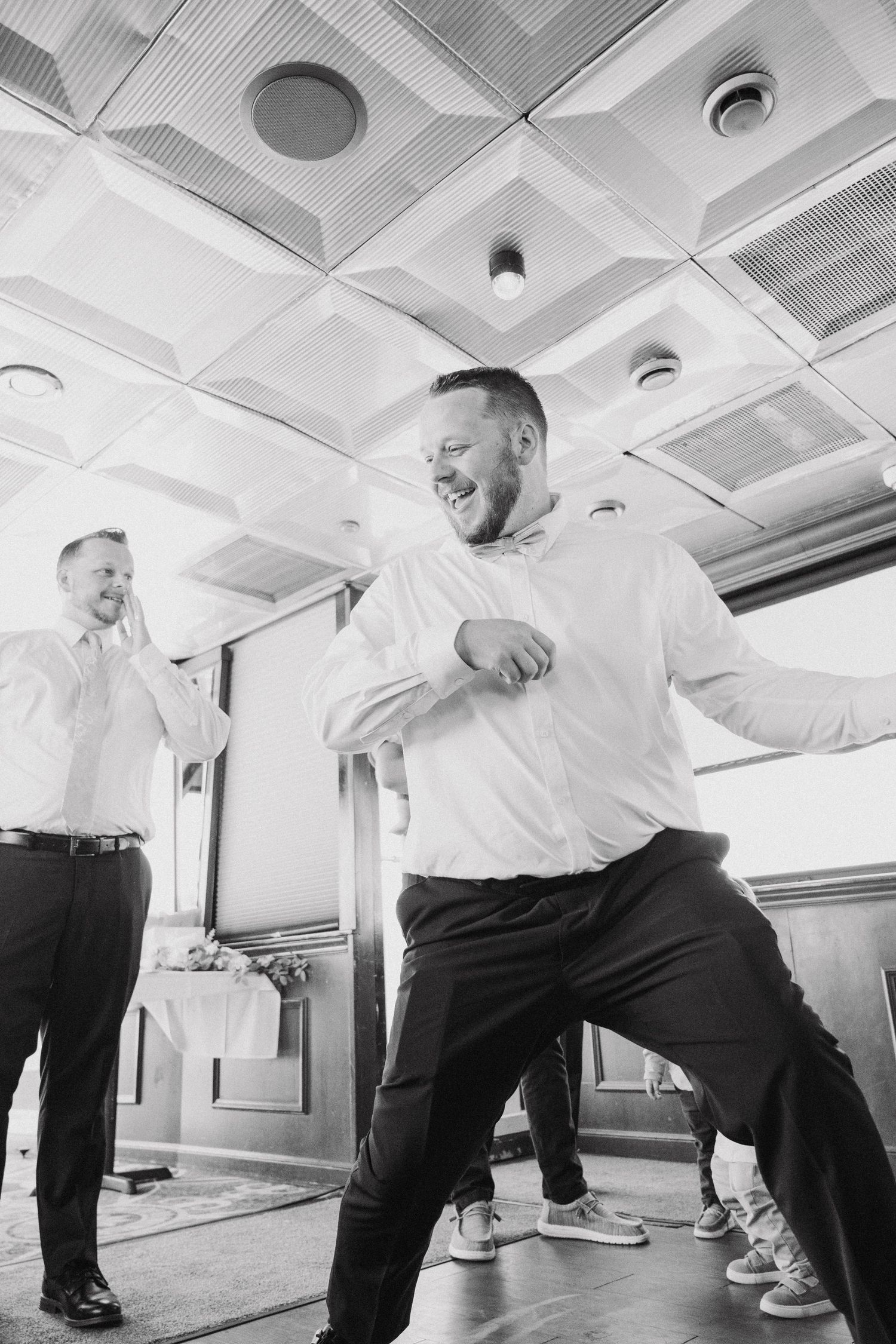 A joyful guest dances energetically at a wedding reception under geometric ceiling tiles.