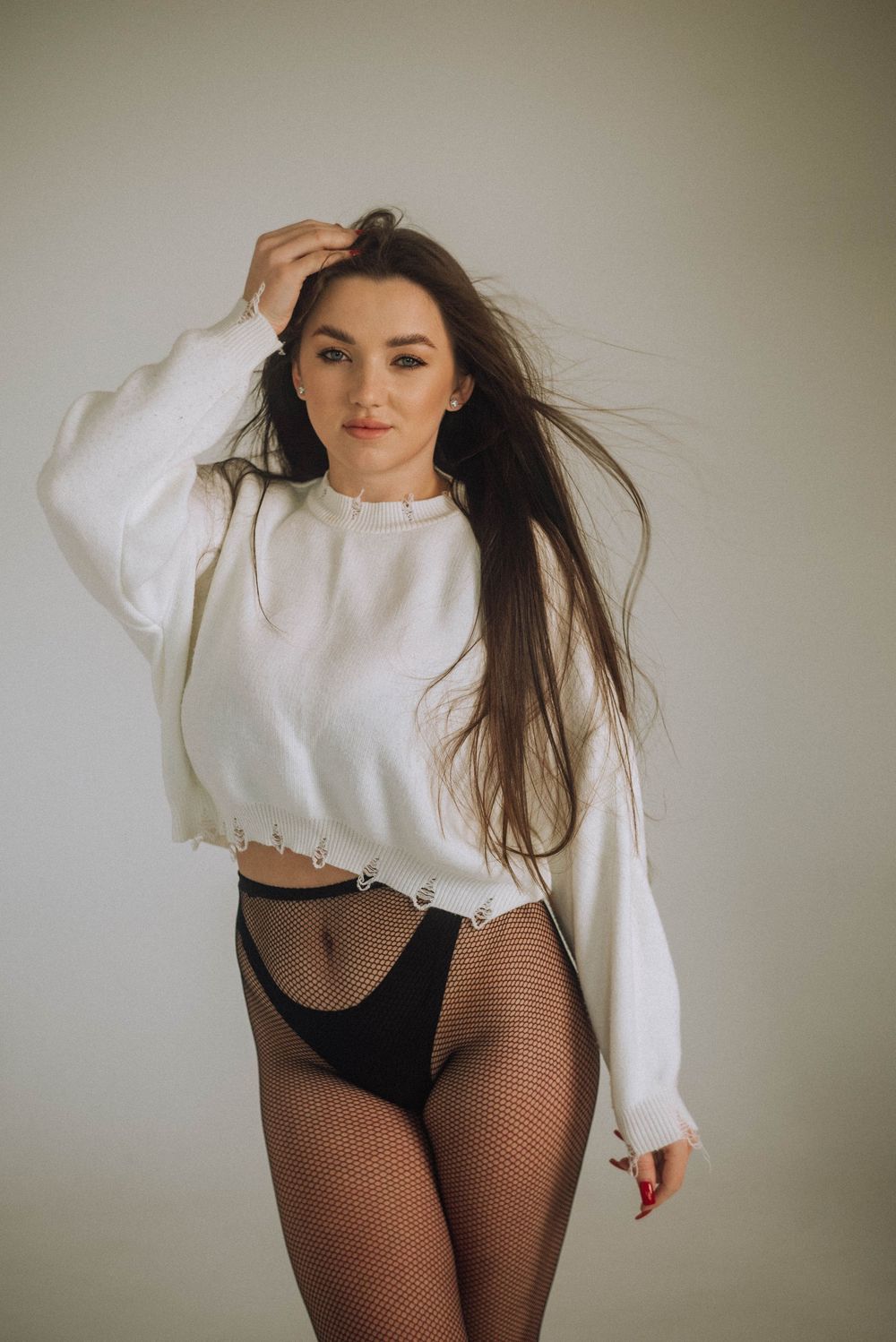 A fashion photo series showing a model in a white sweater and fishnet stockings against a neutral background.