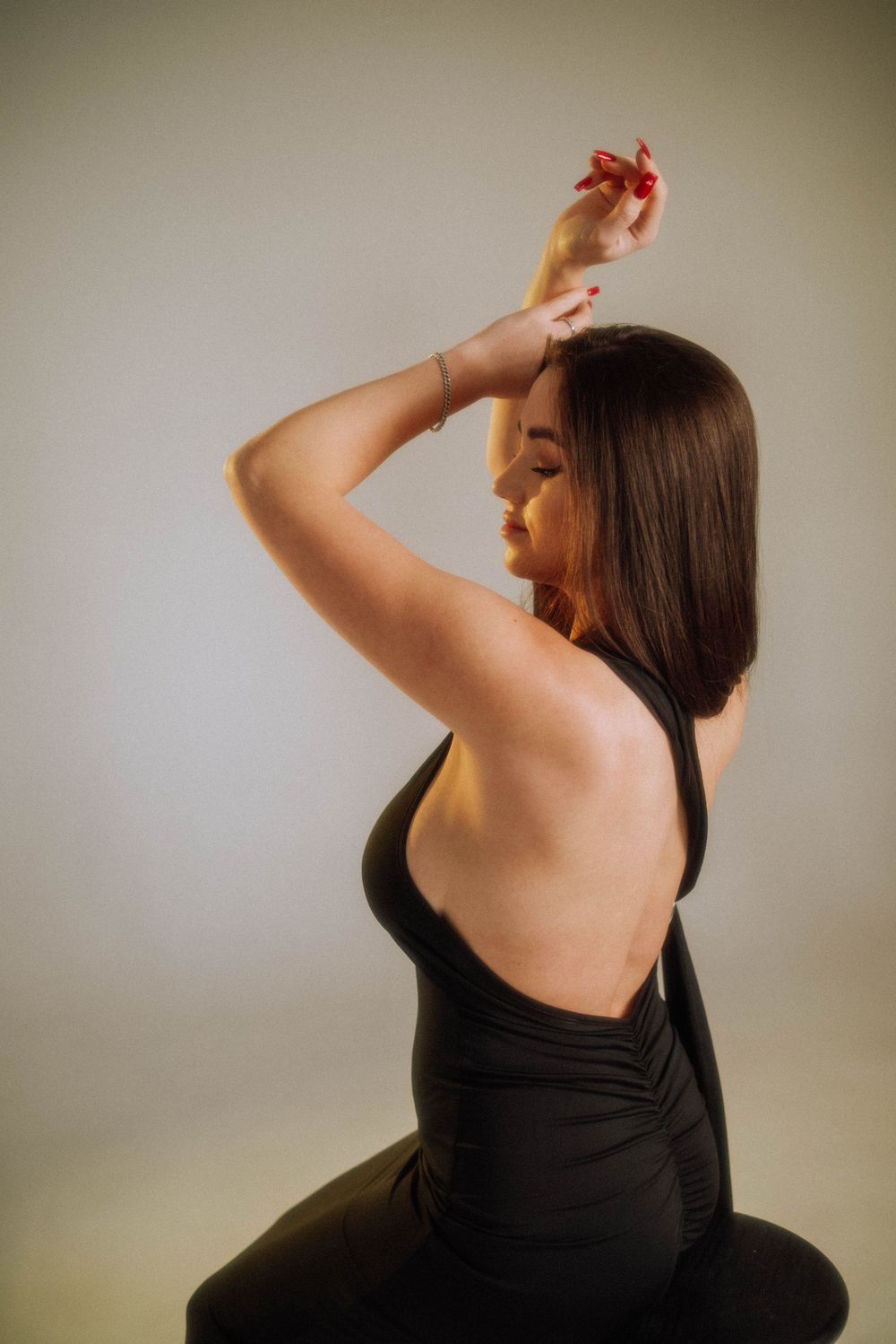 Sensual portrait of a woman in a black dress moving gracefully against a neutral background.