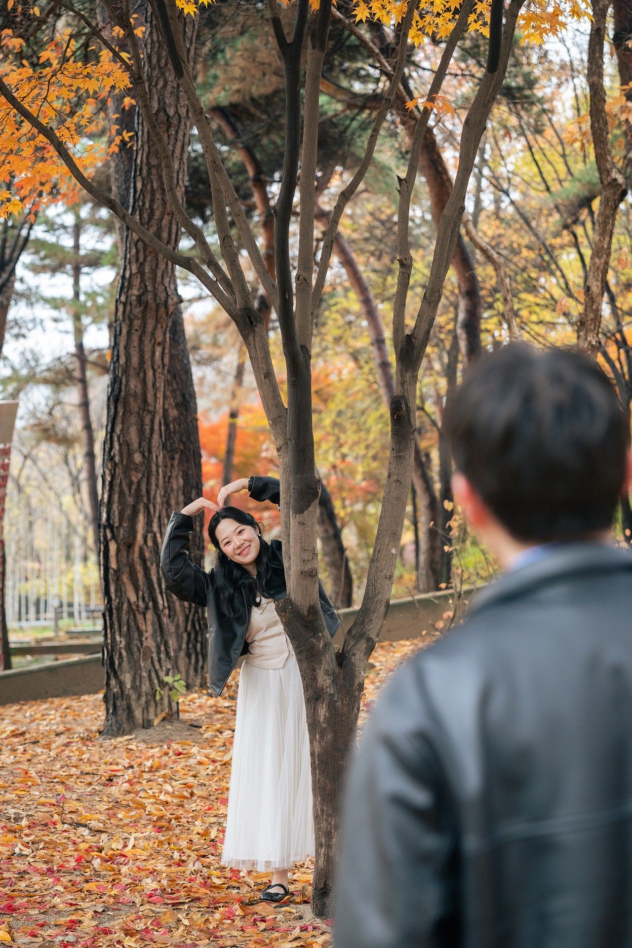 A couple shares a romantic moment in an autumn park setting with fallen leaves and trees creating a warm atmosphere.