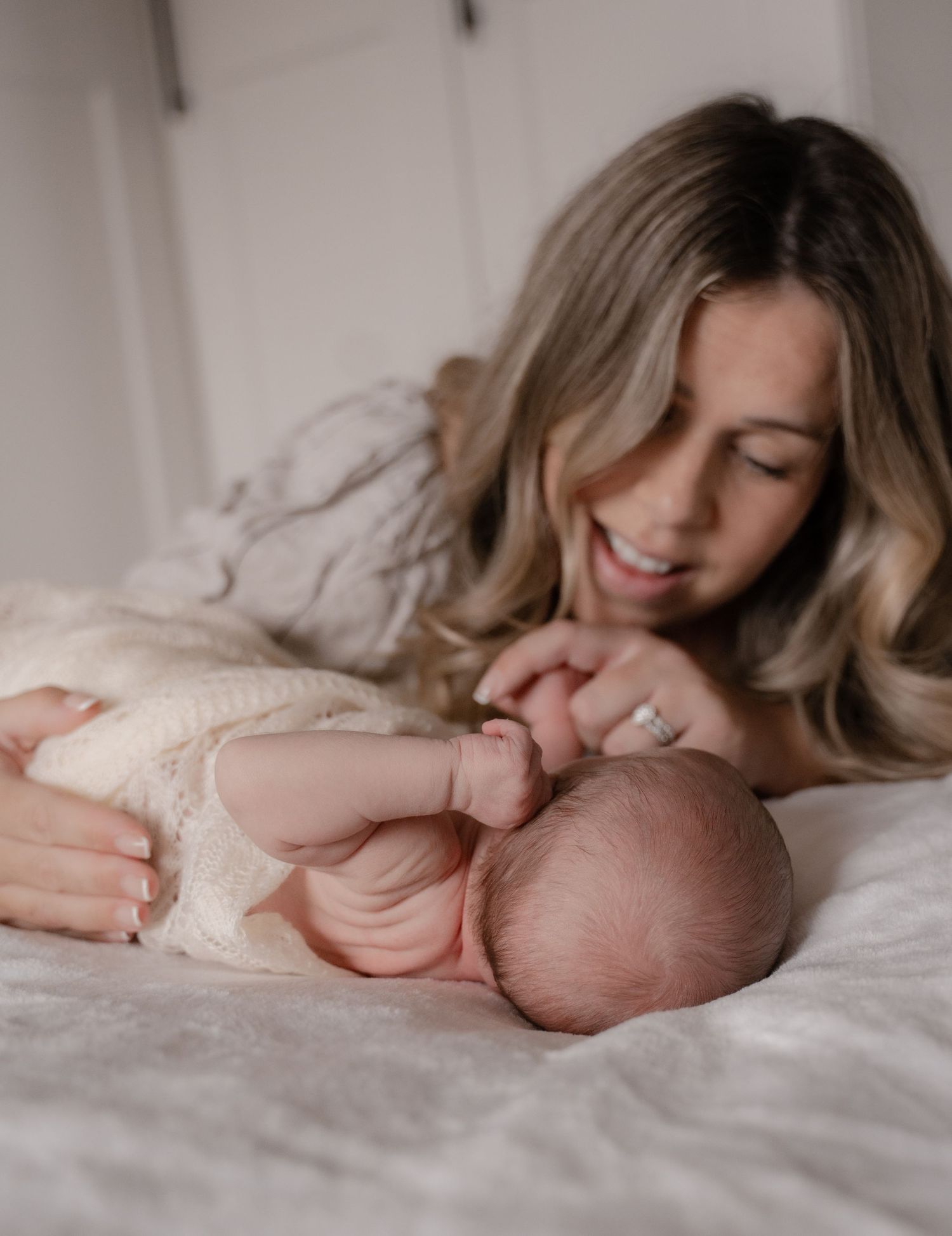 A tender moment between parent and newborn baby lying together on white bedding in soft natural light.