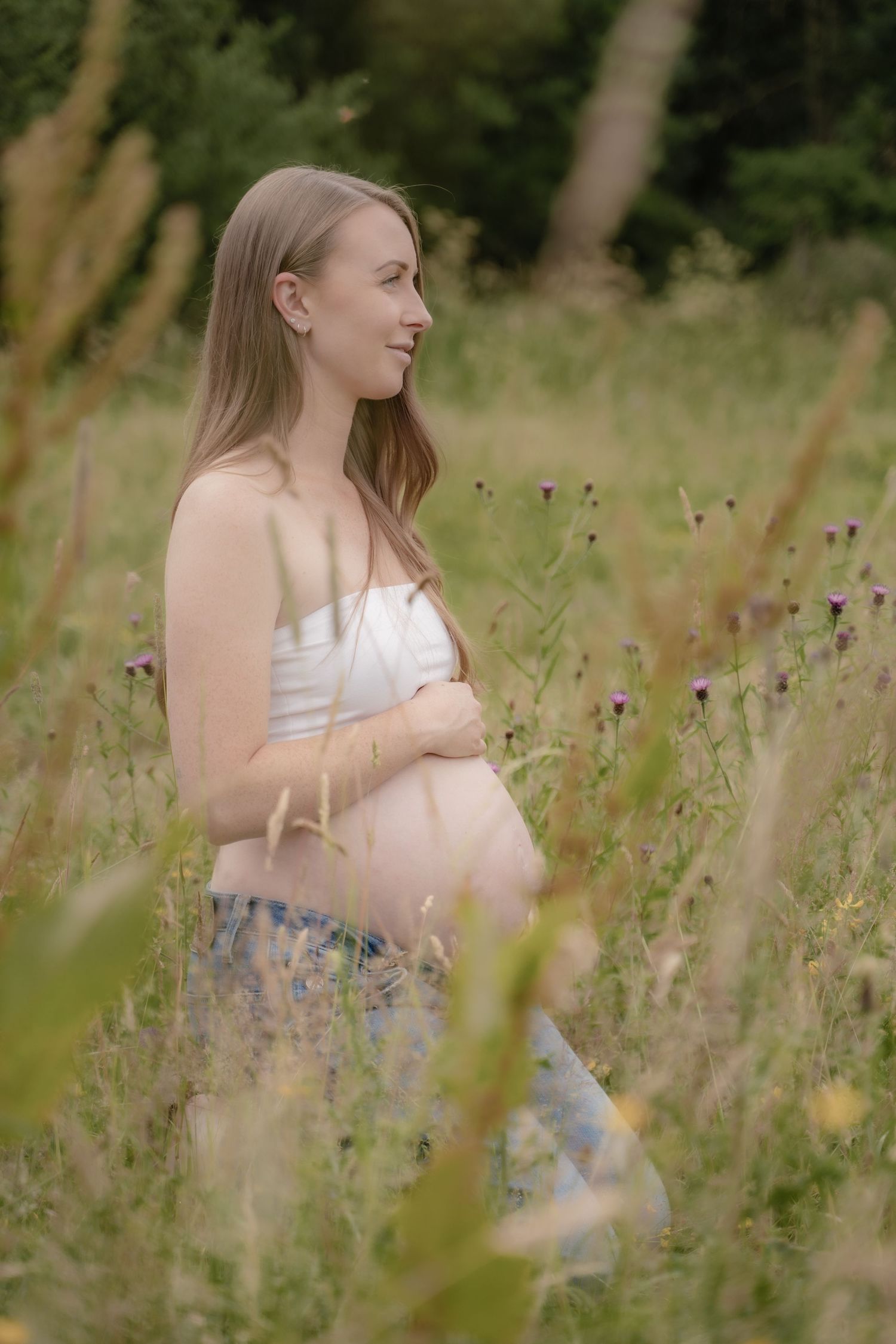 A woman in a white top sits thoughtfully in a summer meadow surrounded by purple wildflowers and tall grass.