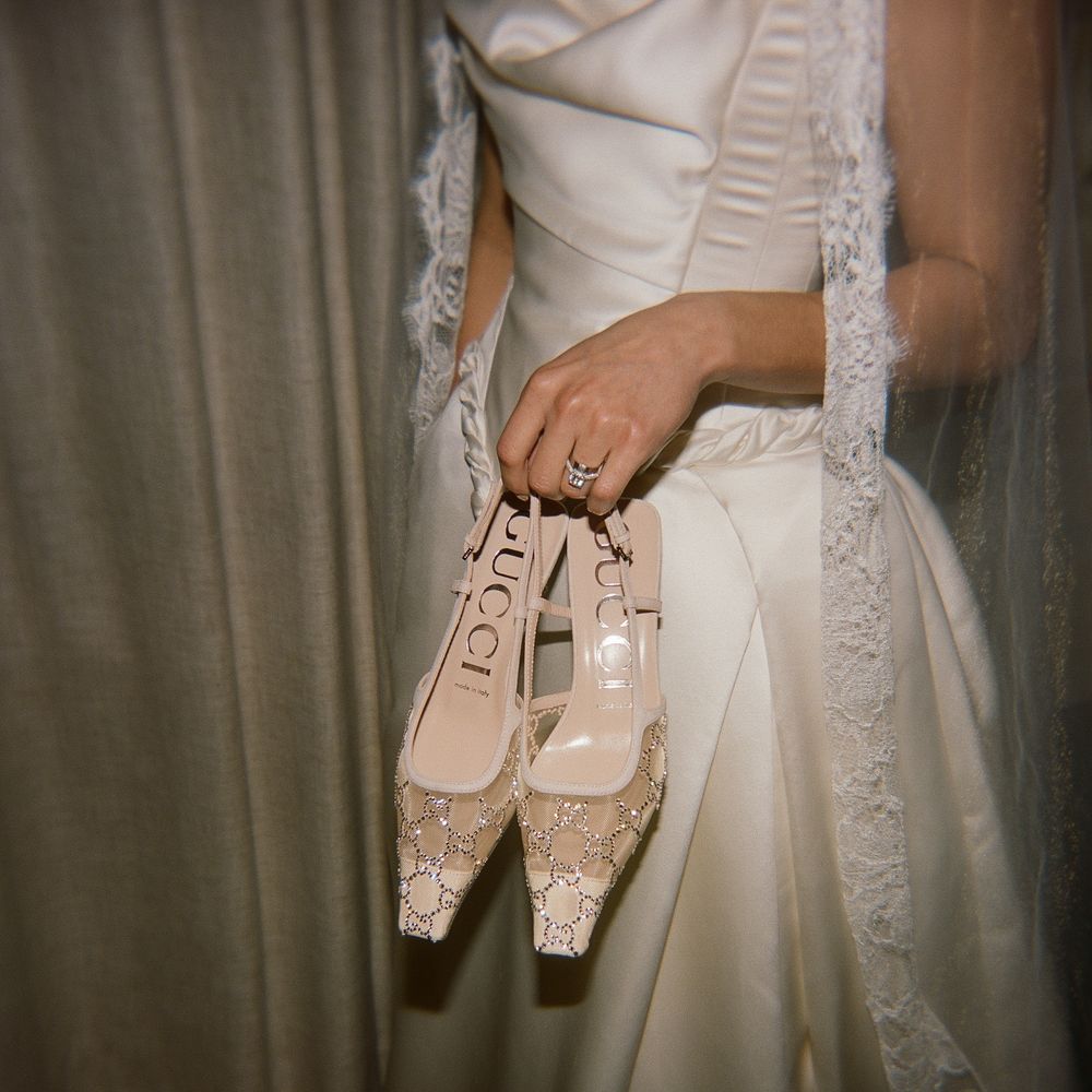 Close-up of delicate lace wedding shoes held against a white dress.