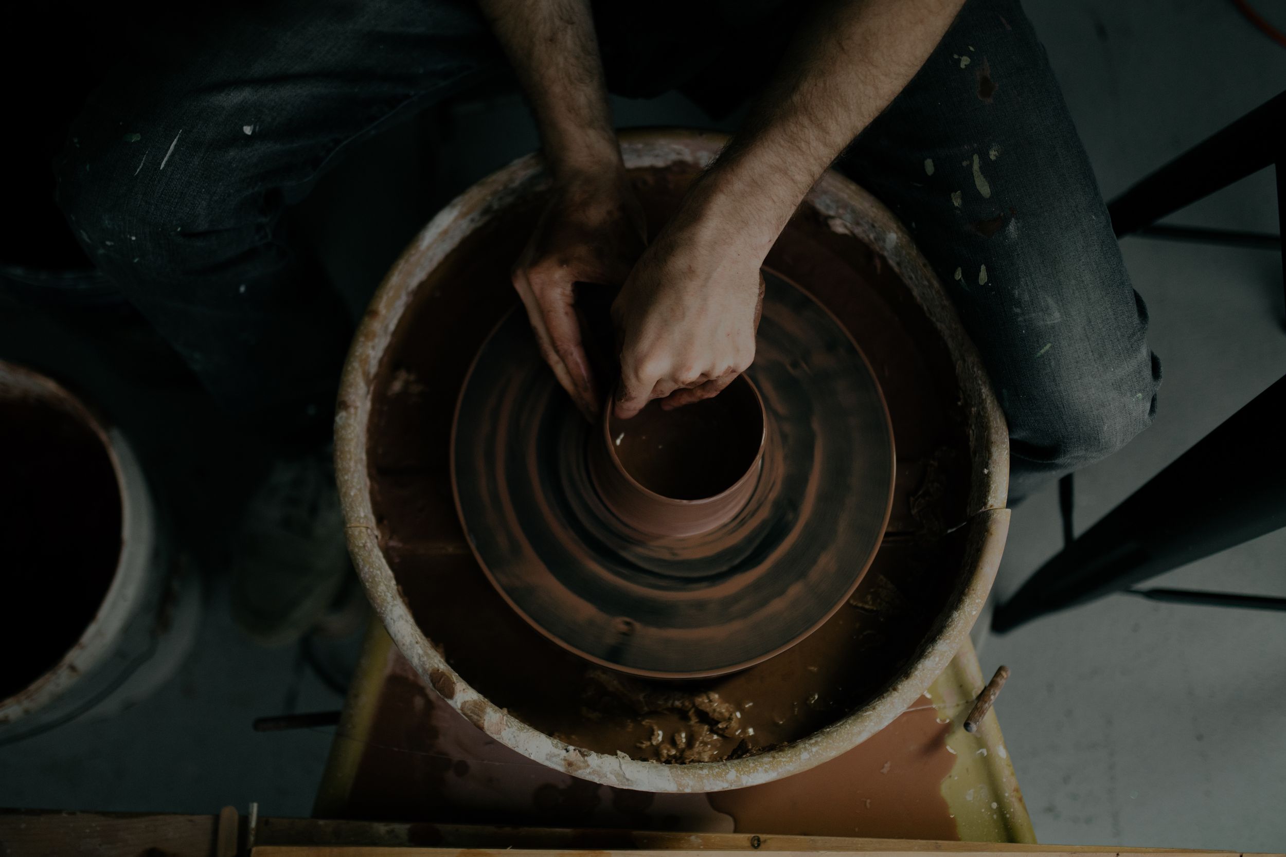 Hands shape wet clay on a pottery wheel during a ceramic making process, creating a handmade vessel.
