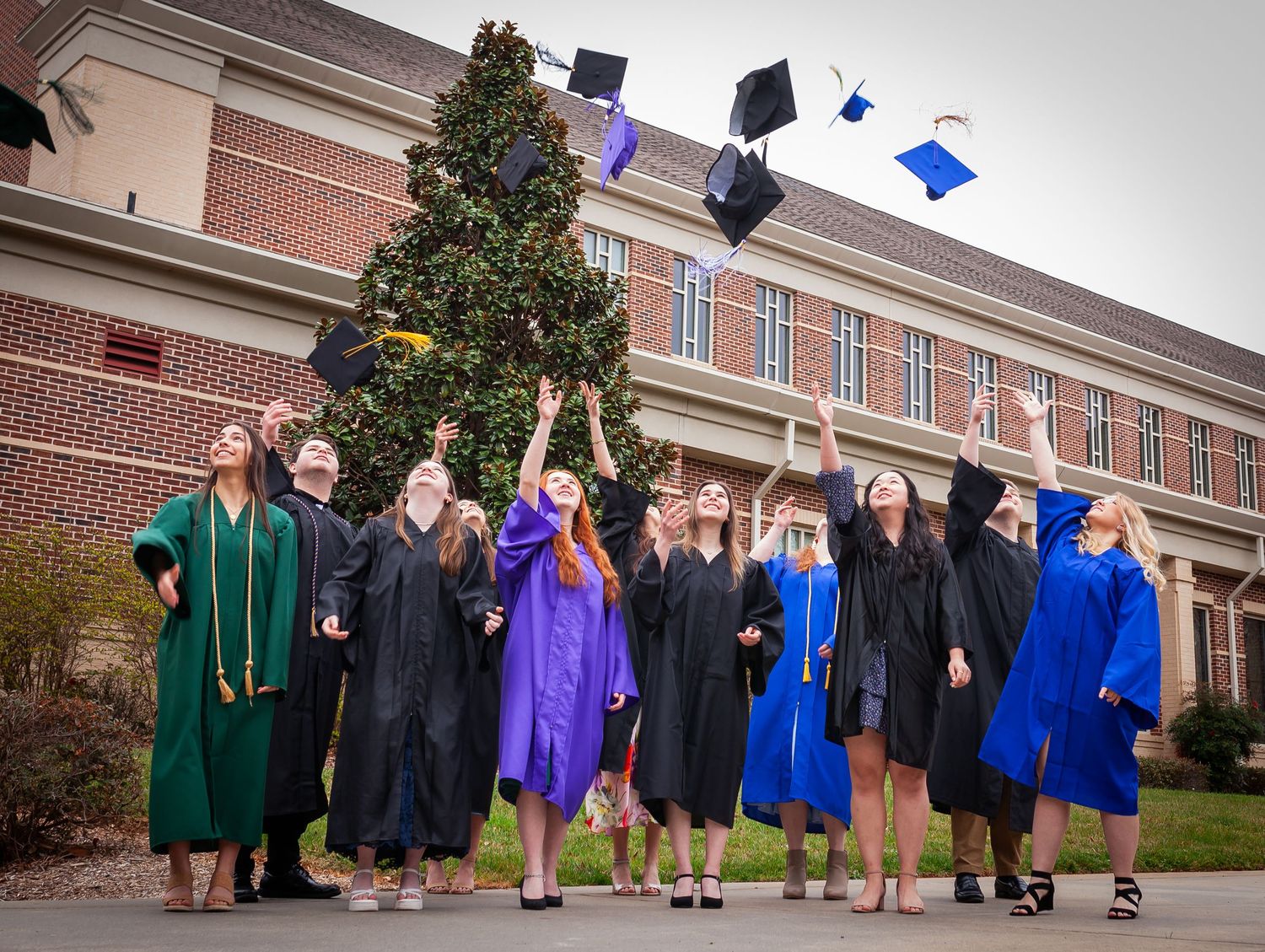 Excited graduates tossing caps in the air outside brick university building.