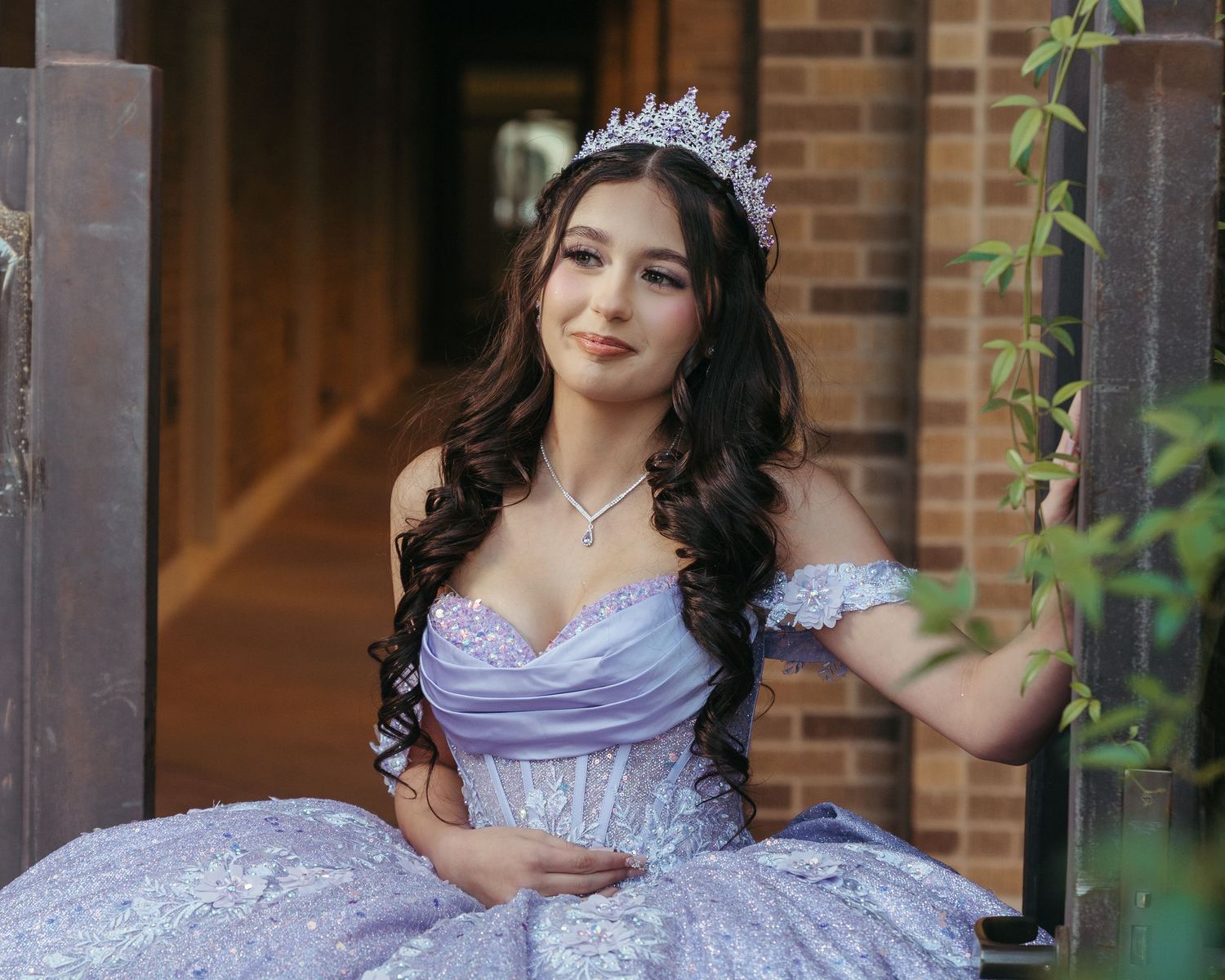 Young woman wearing a purple quincerñera dress smiling in doorway.