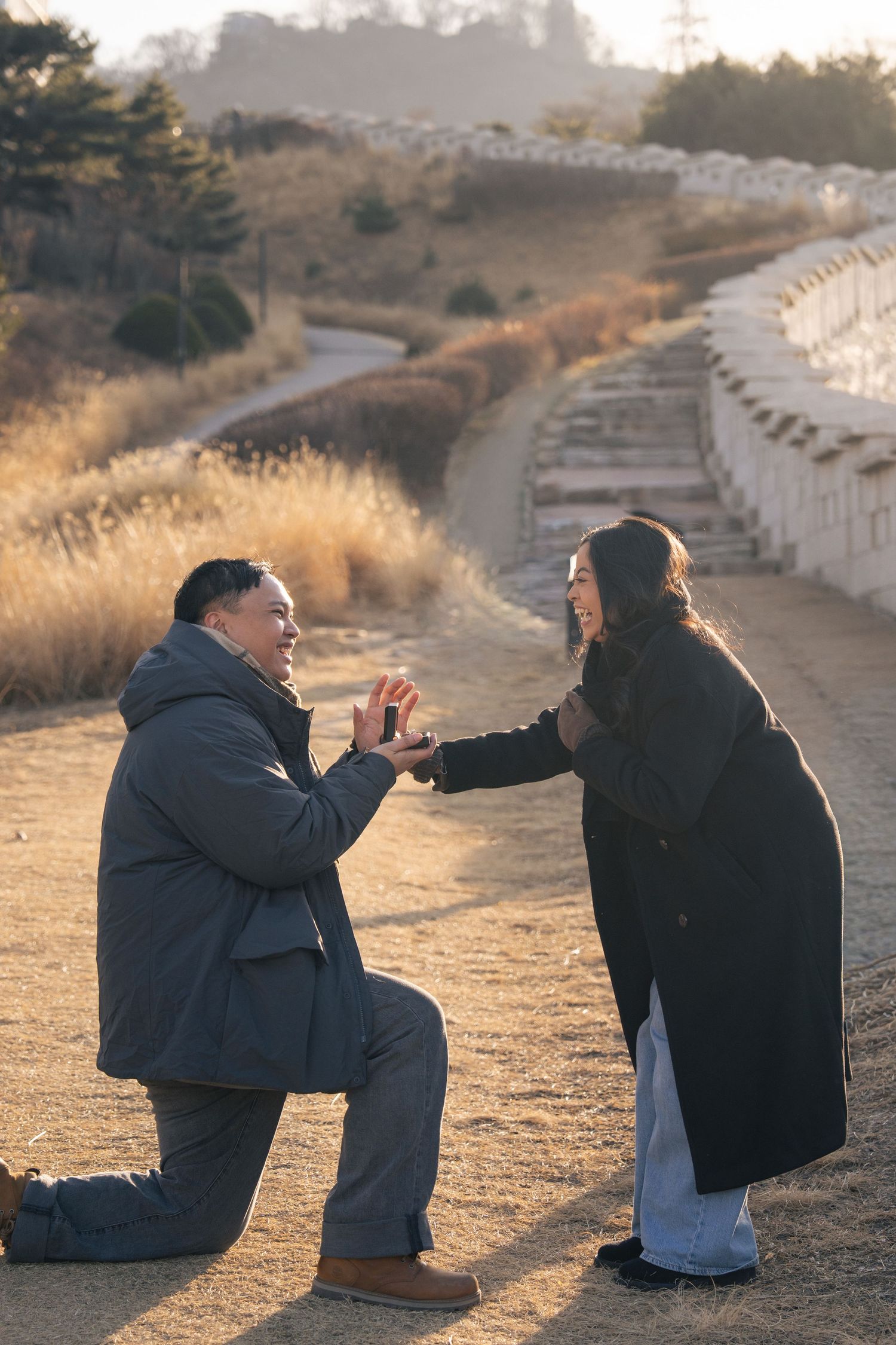 A romantic proposal moment captured on a winding dirt path during golden hour with scenic hills in the background.