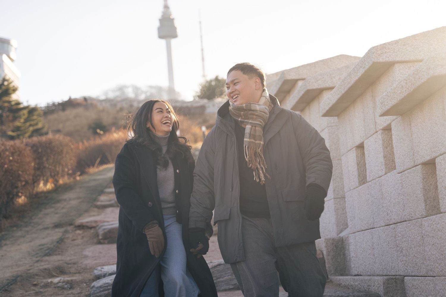 A couple in dark winter clothing stands close together outdoors during golden hour lighting.