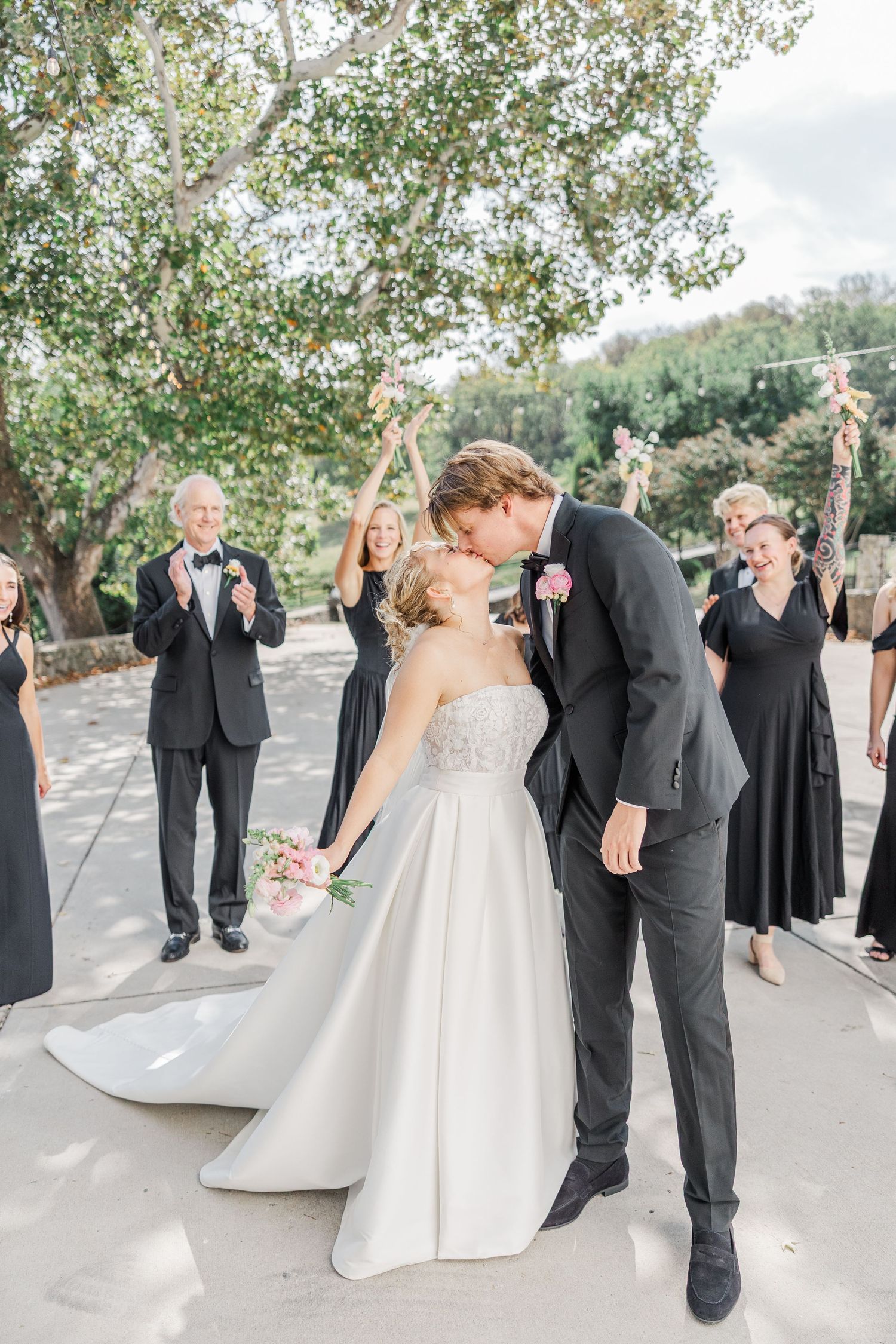 Wedding party celebrating with joyful poses and interactions on an outdoor stone pathway.
