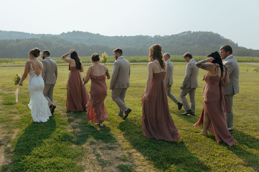 A group of people in brown dresses walking together across a sunlit grassy field on a summer day.