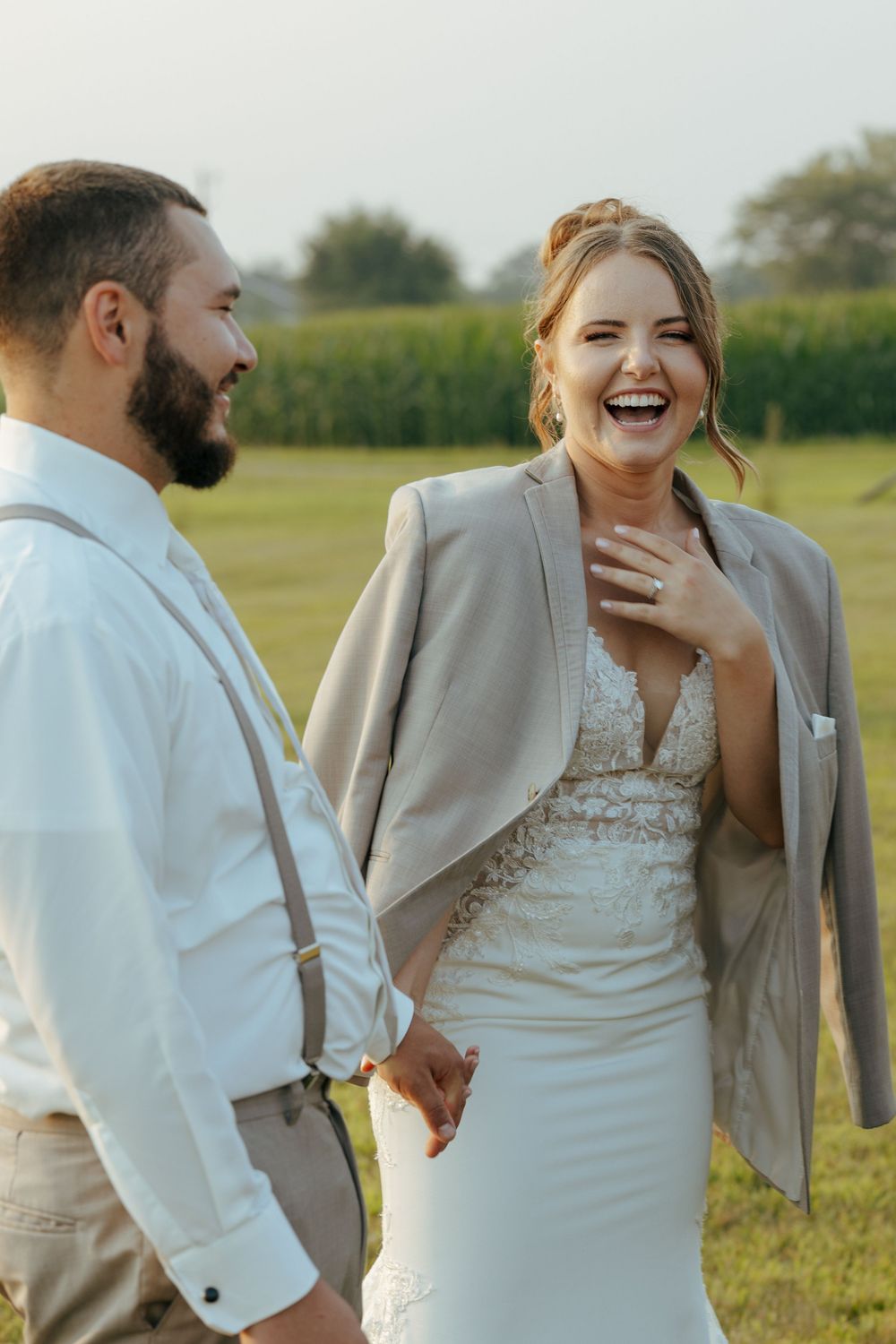 A couple shares joyful laughter in a grassy field during their wedding photo session.