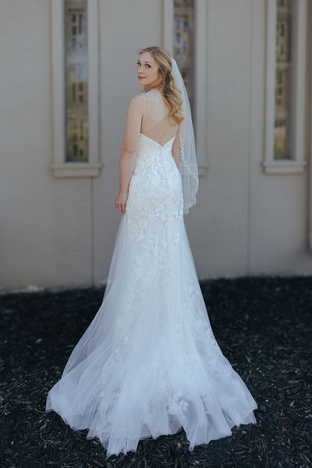 Flowing white wedding dress with delicate lace details and train photographed from behind.