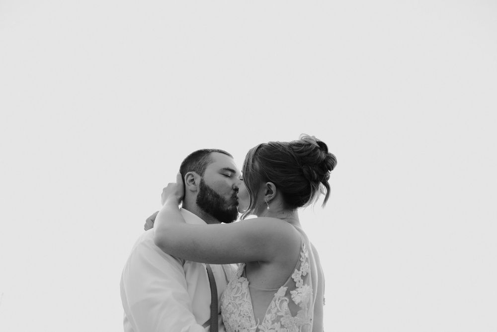 A tender black and white photograph of a romantic embrace between newlyweds against a light background.