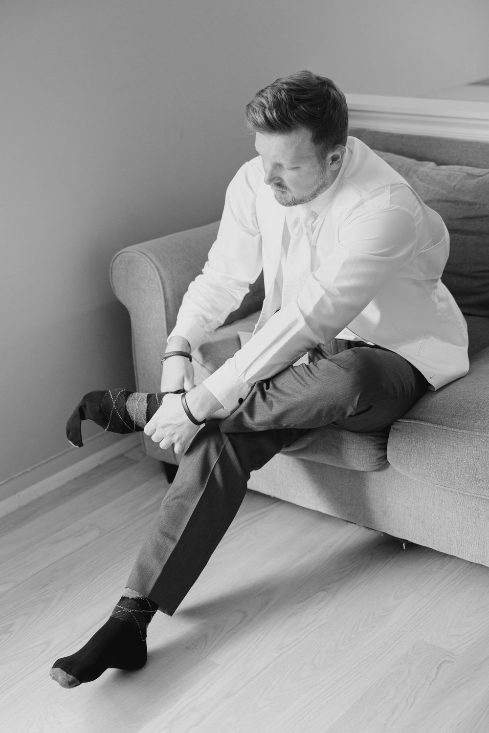 A sequence of black and white photos showing someone putting on socks while sitting on a light-colored couch.