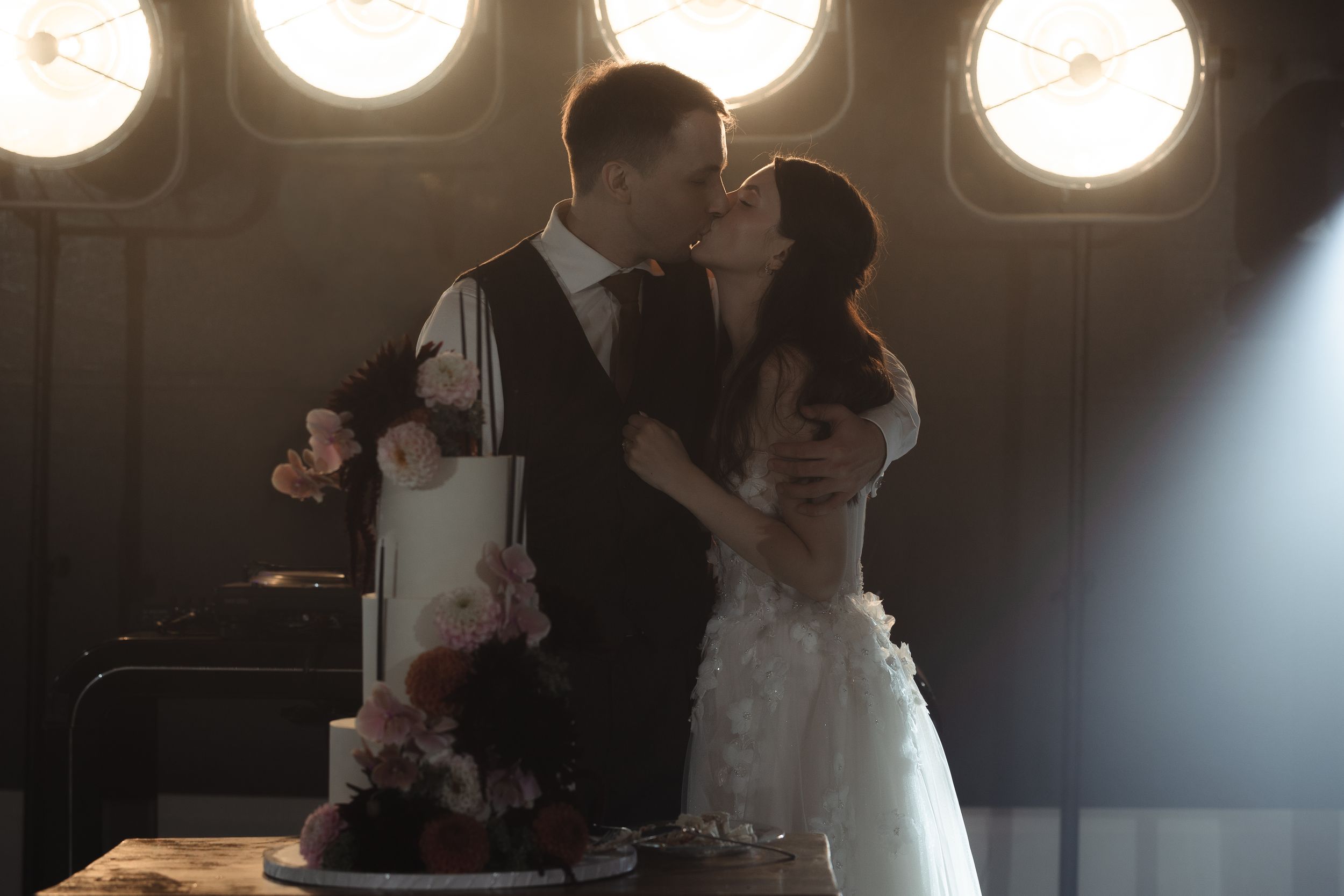 A wedding couple dances together on a dimly lit dance floor with dramatic lighting and smoke effects in the background.
