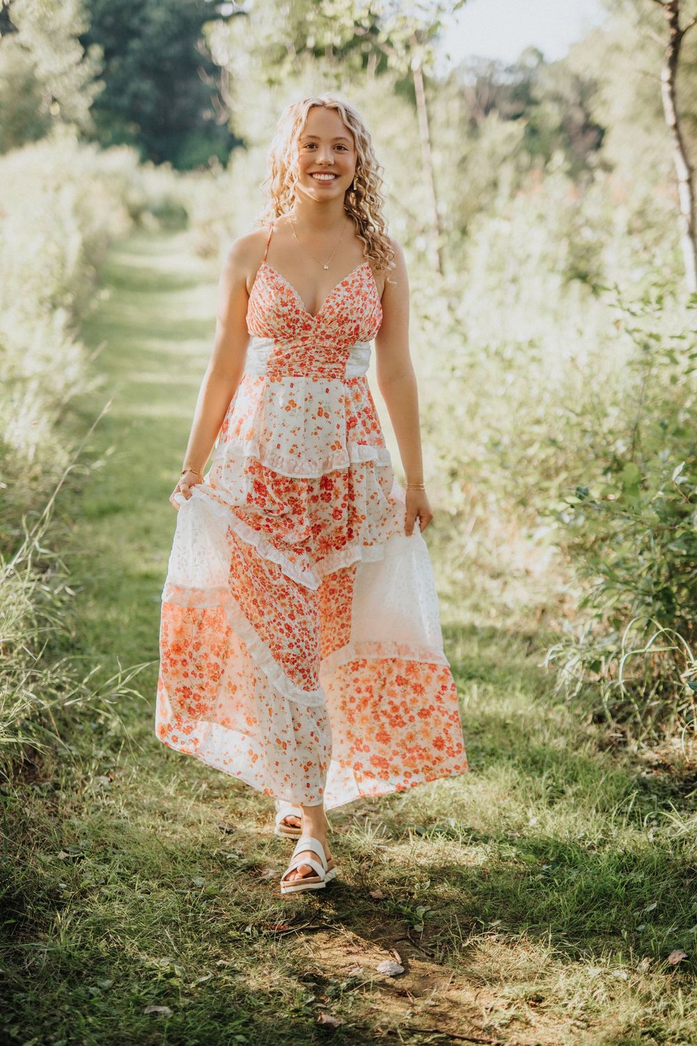 A flowy white and coral floral dress sways in the sunlight along a grassy outdoor path.