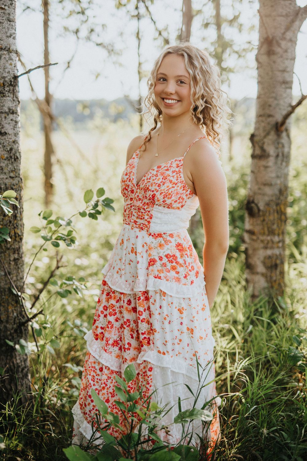A floral sundress is captured in a dreamy outdoor photoshoot among birch trees and tall grass at golden hour.
