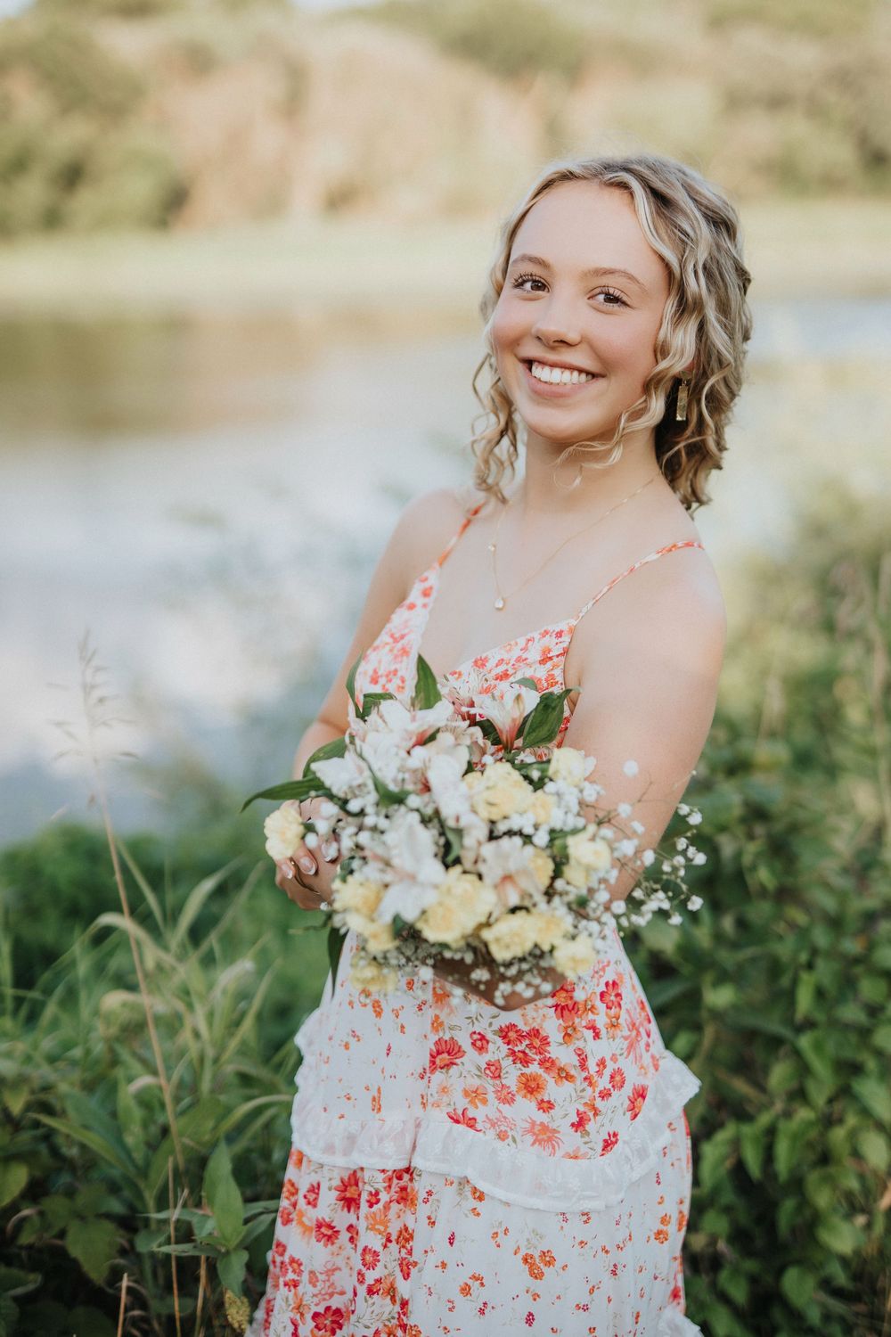 A floral sundress glows in golden sunlight as a bouquet of pastel flowers is held against a natural outdoor backdrop.