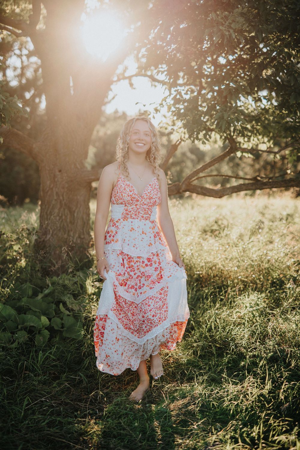 A flowing red and white floral dress catches sunlight in a dreamy outdoor portrait session at golden hour.