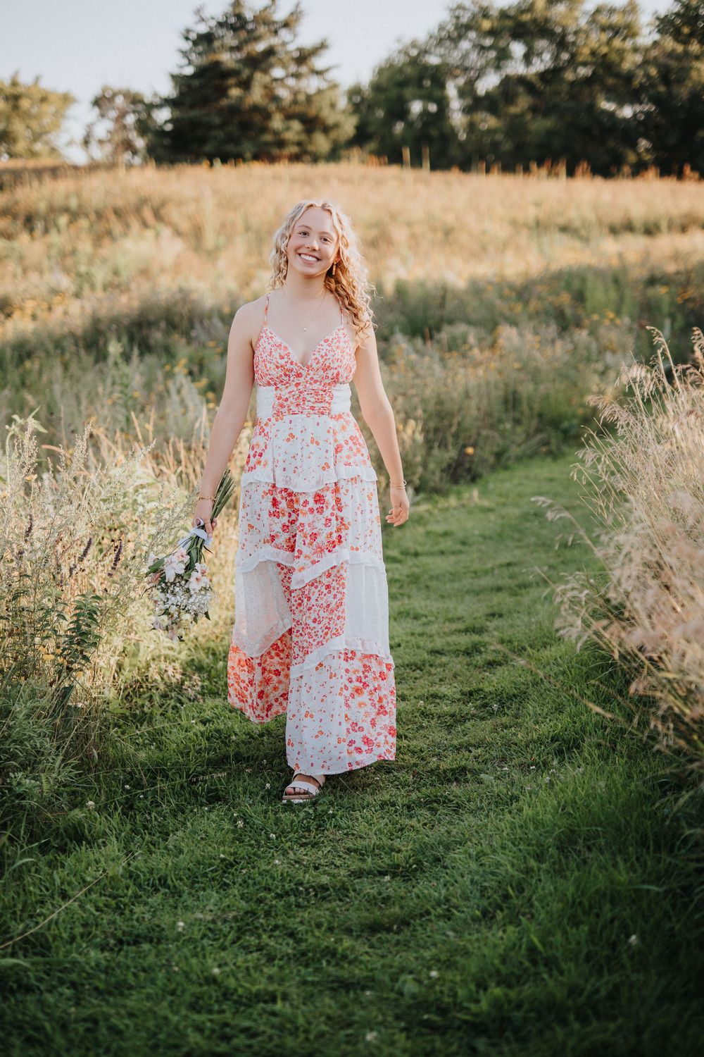 A flowing white and coral dress stands out against a golden-hour meadow backdrop.