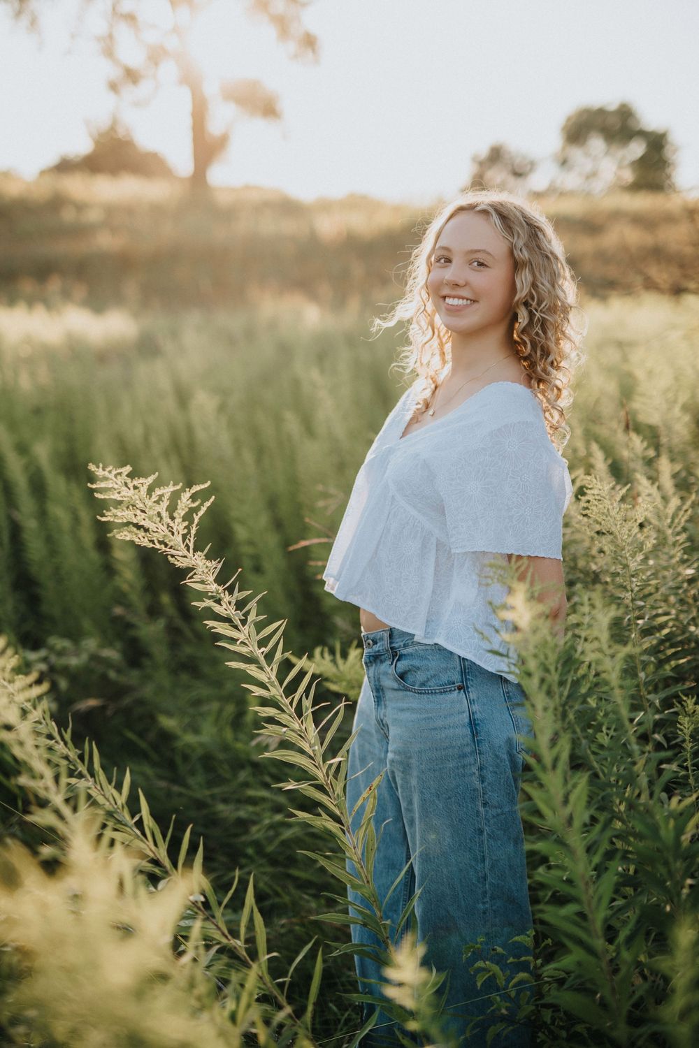 A dreamy golden hour portrait in a field of tall grass and wildflowers with soft sunlight filtering through.