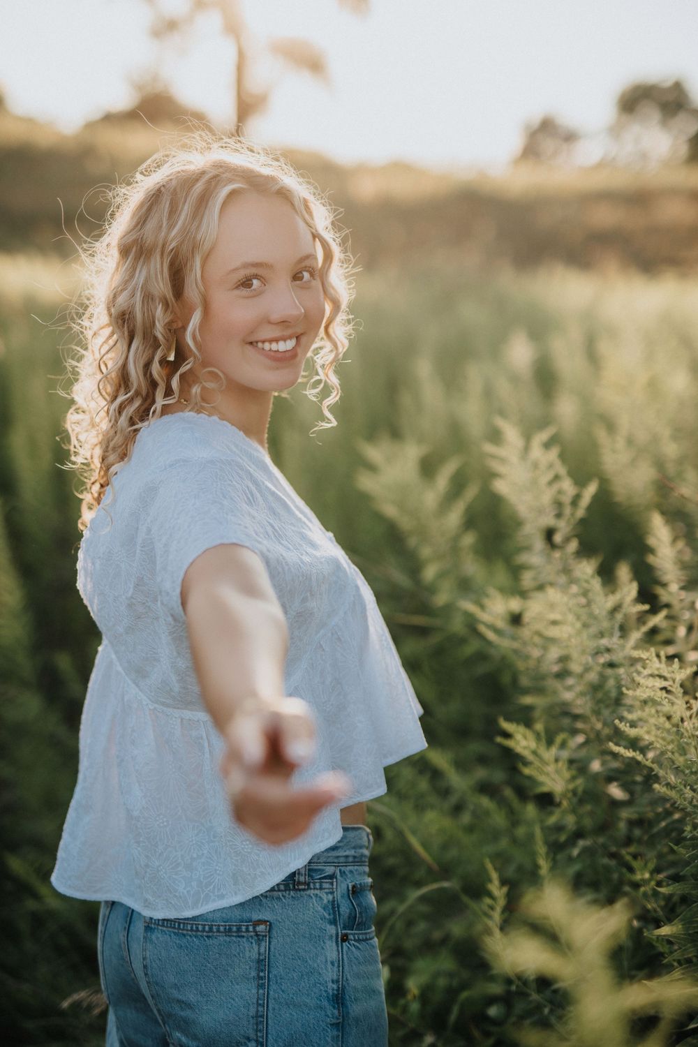 Light blue top and denim outfit captured in warm sunset lighting among tall green ferns.