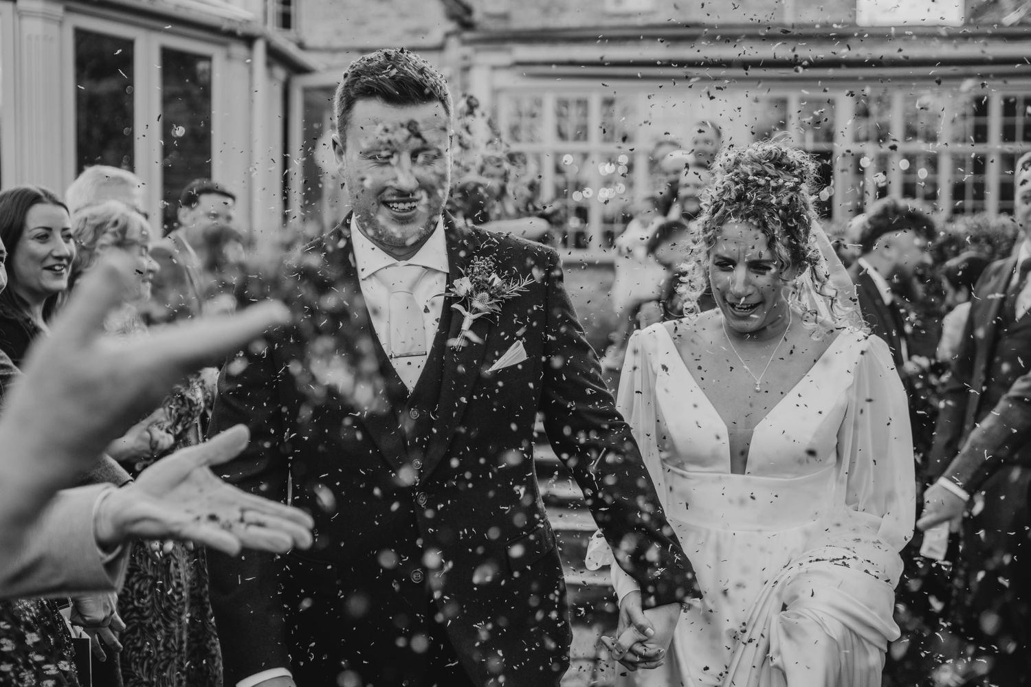 Wedding guests laugh and celebrate during an outdoor reception as confetti fills the air around them.
