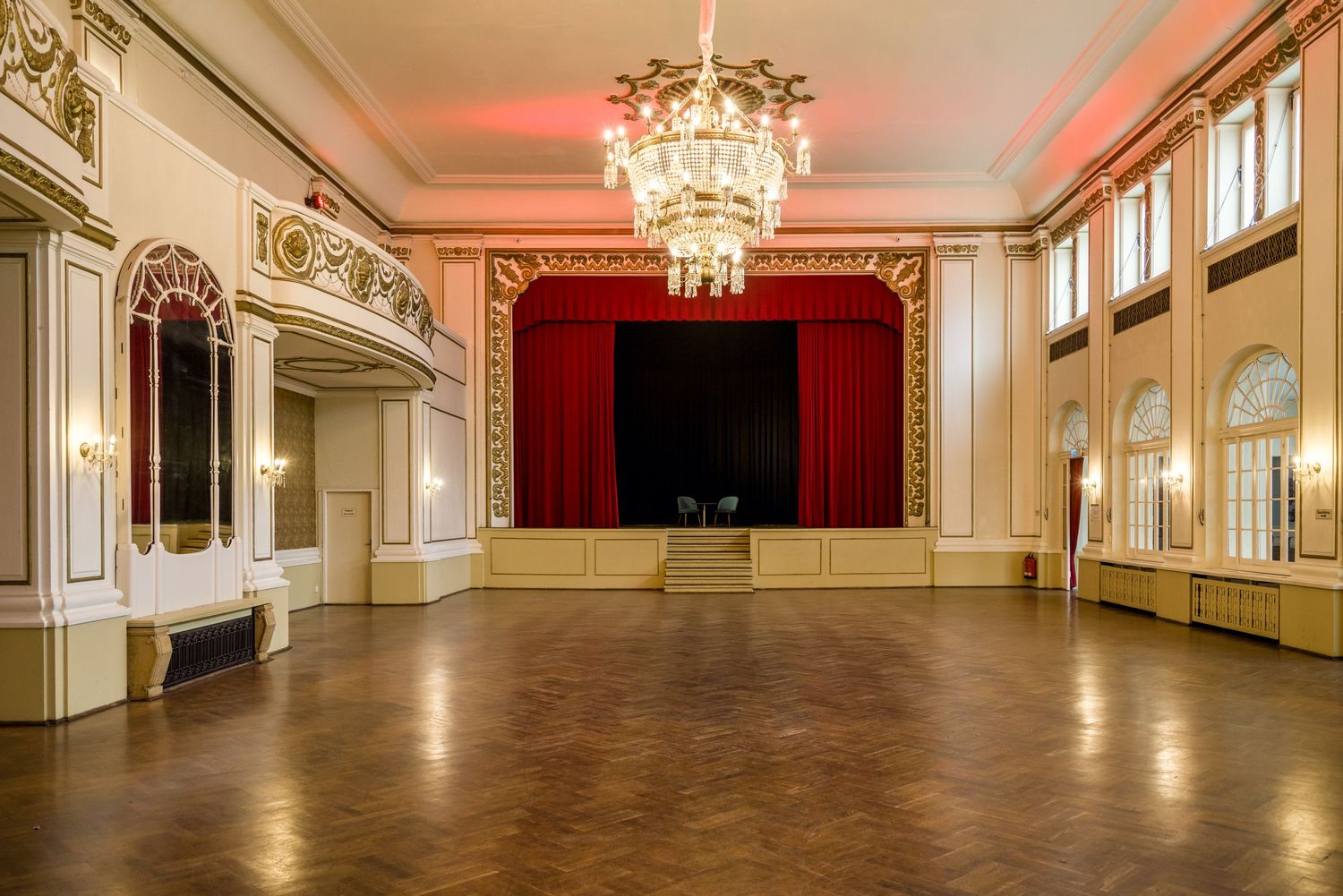 Luxurious banquet hall with crystal chandeliers, red accents, and decorative ceiling details in panoramic view. Parkhotel | Dresden