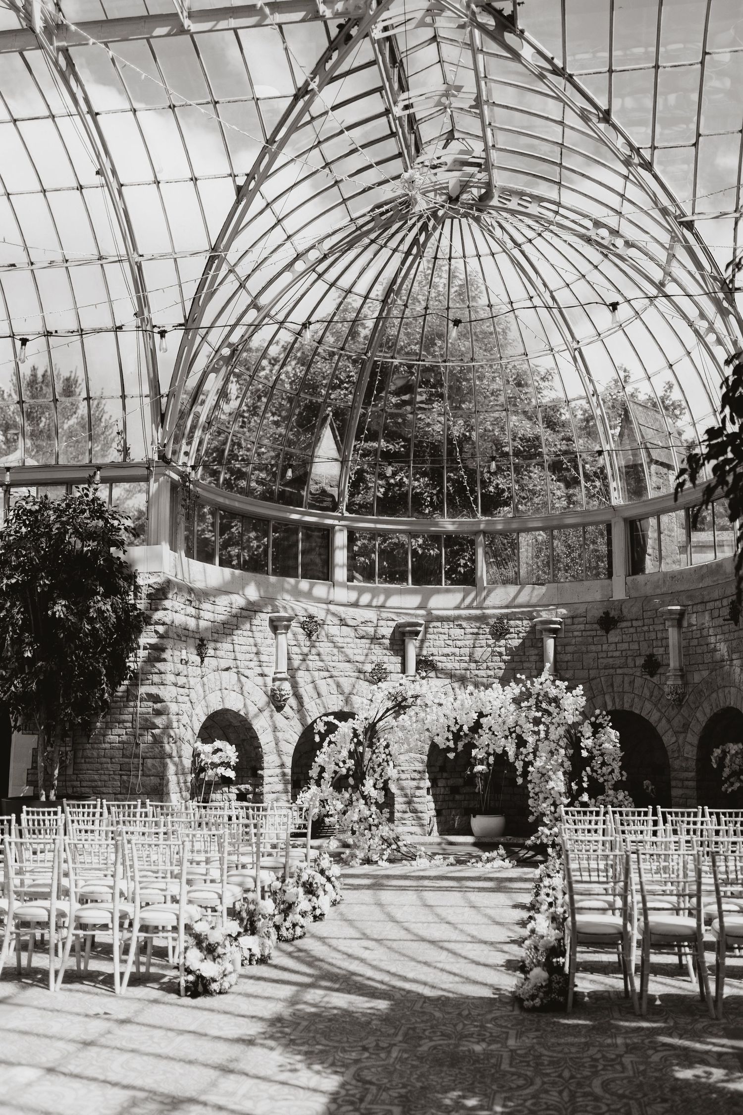 Black and white photo series showing an indoor wedding venue with arched glass ceiling and rows of white chairs set up for ceremony.