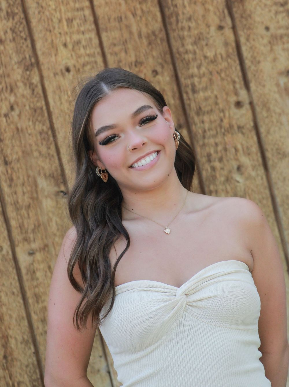 A portrait showing a bright smile wearing a white strapless top against a wooden wall background.