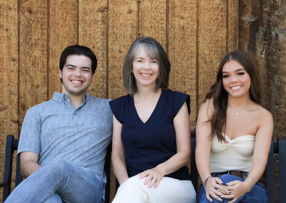 Three people sitting together on bench against wooden wall background.