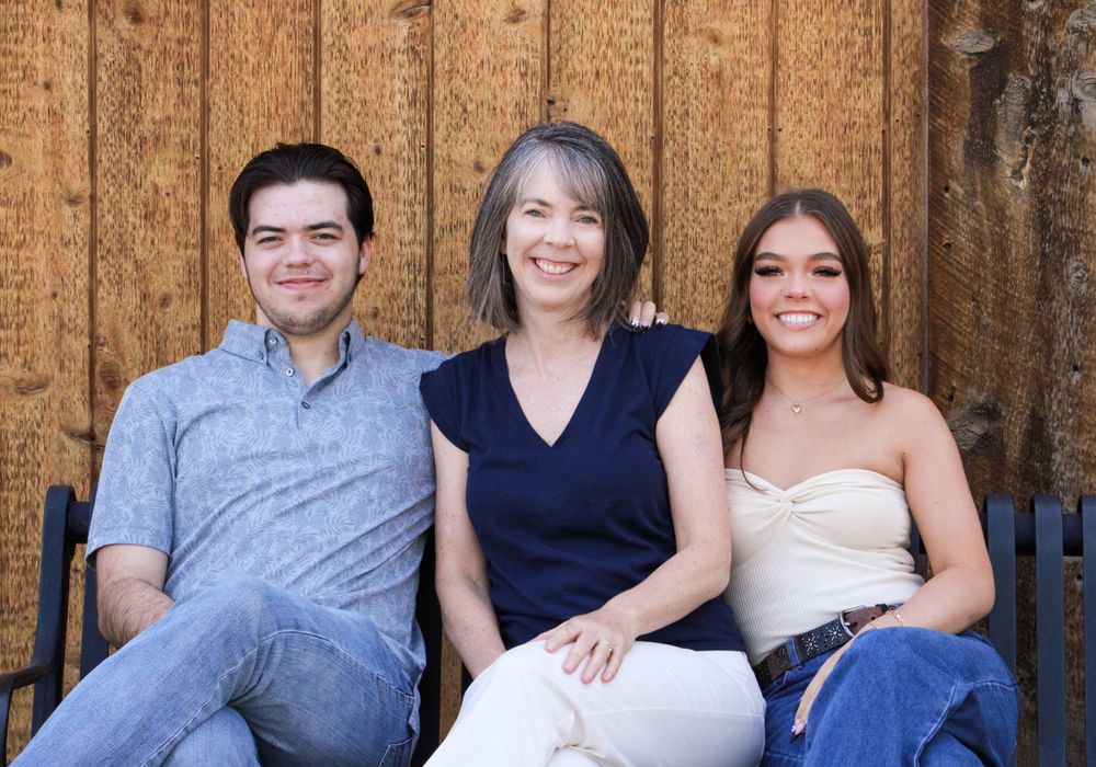 Three people sitting together on wooden bench against rustic wooden wall background.