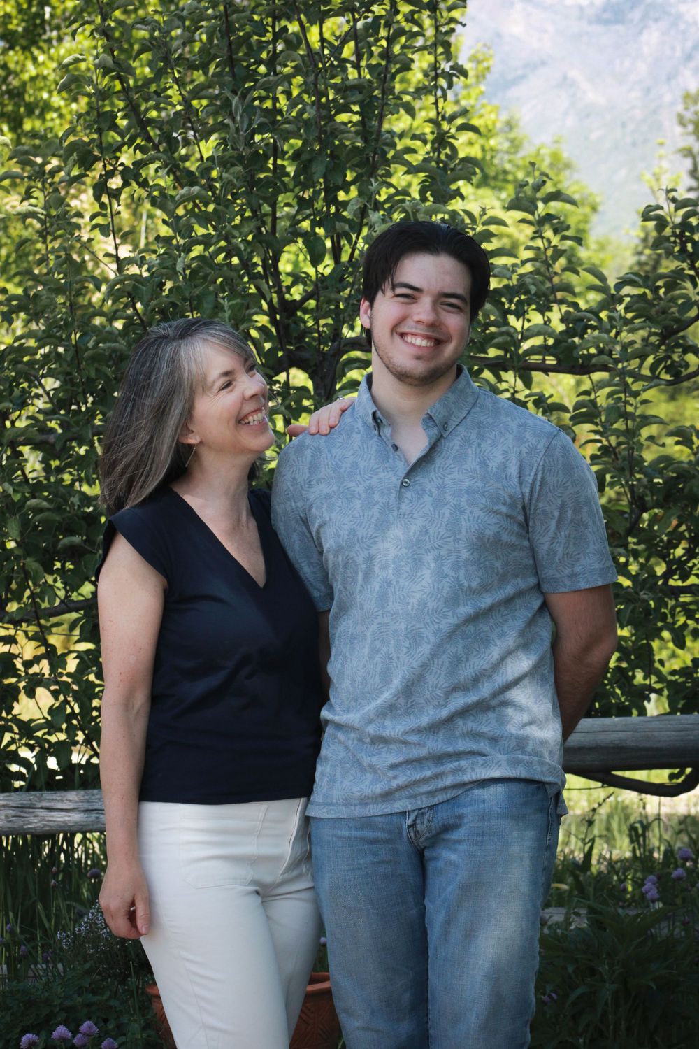 Two people sharing a candid moment outdoors with greenery and mountains behind them.