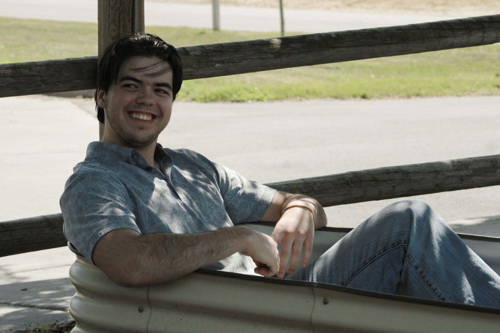 Person relaxing on outdoor bench in casual attire with dappled sunlight.
