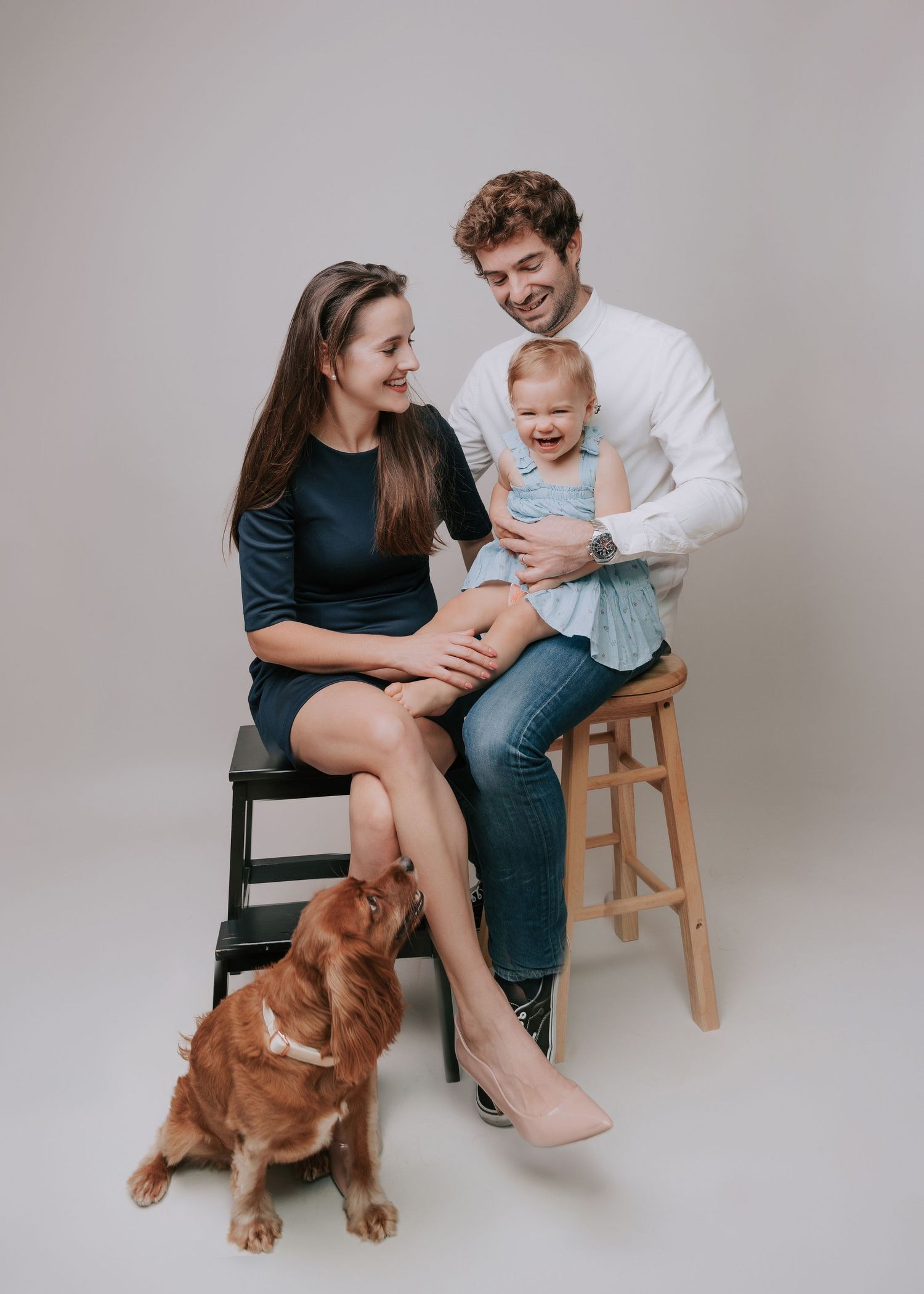 family of 3 and a dog interacting and laughing dressed in shades of blue in studio backdrop