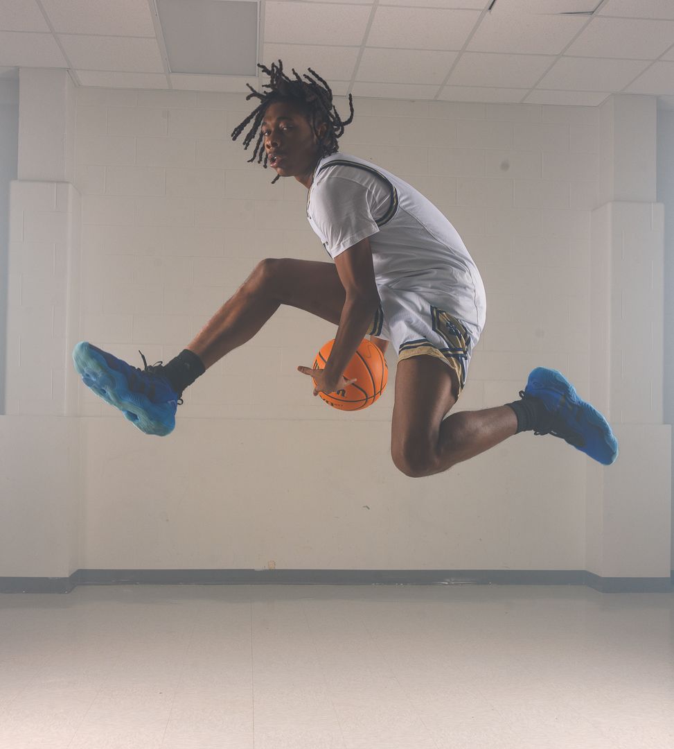 Athletic figure leaping in mid-air while holding a basketball in an indoor setting.