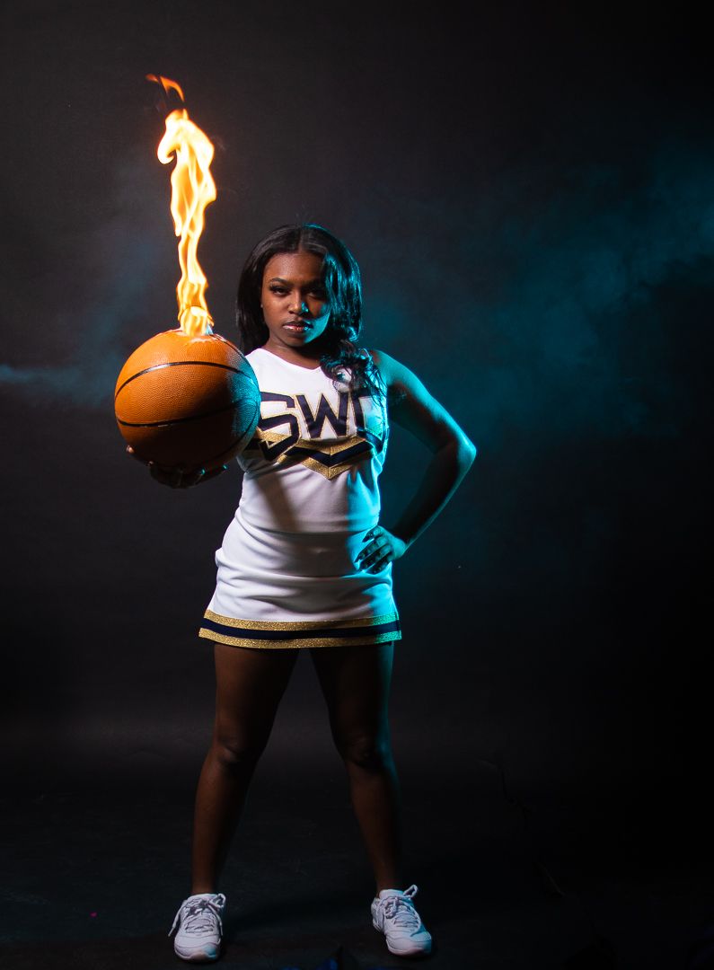A cheerleader holds a flaming basketball in dramatic blue and orange lighting.
