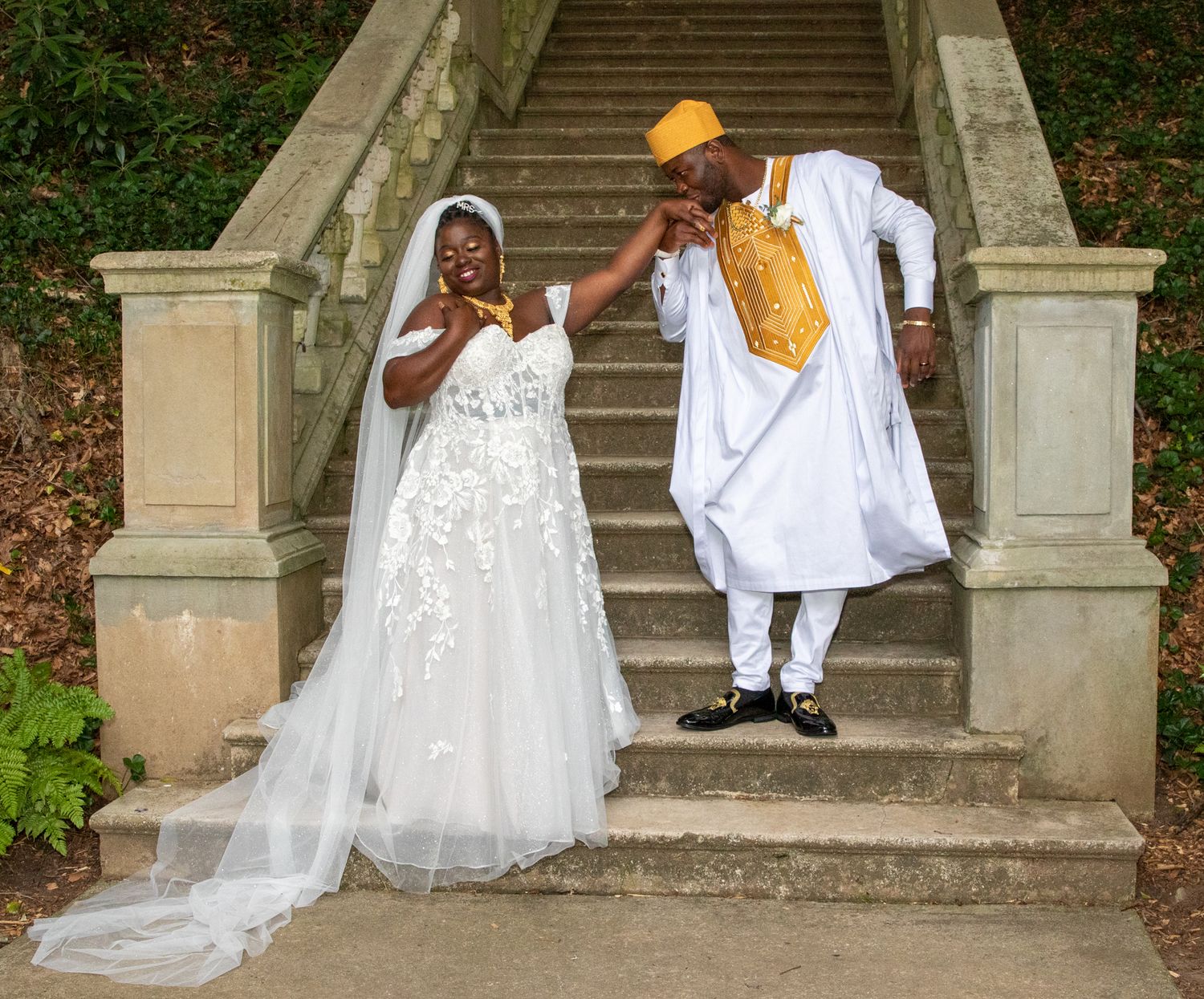 A bride and groom share a joyful moment on stone steps in traditional wedding attire.