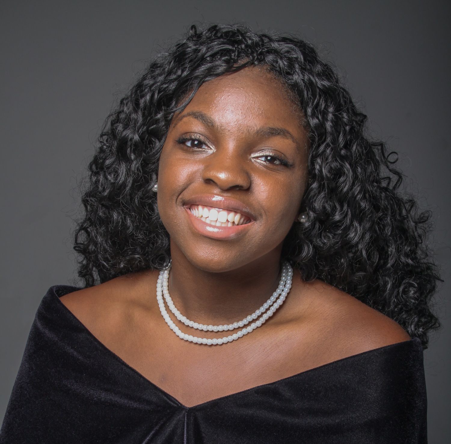 An elegant portrait featuring curly hair, pearl necklace, and off-shoulder black dress.