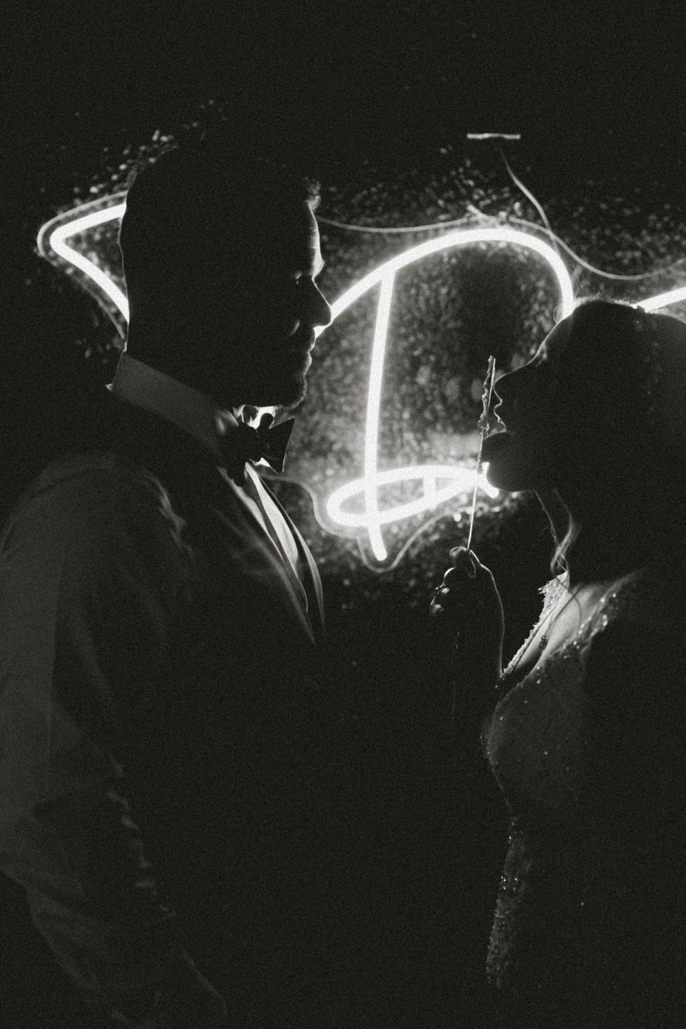 Black and white silhouette of a couple facing each other with glowing neon light behind them.