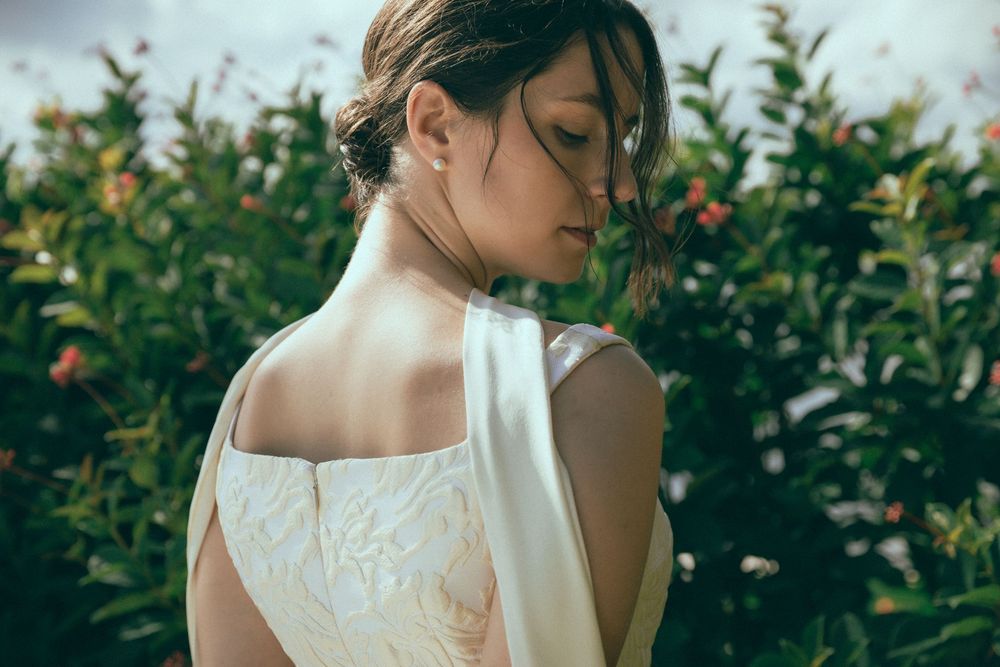 Elegant bride in backless lace wedding dress surrounded by lush green garden foliage.