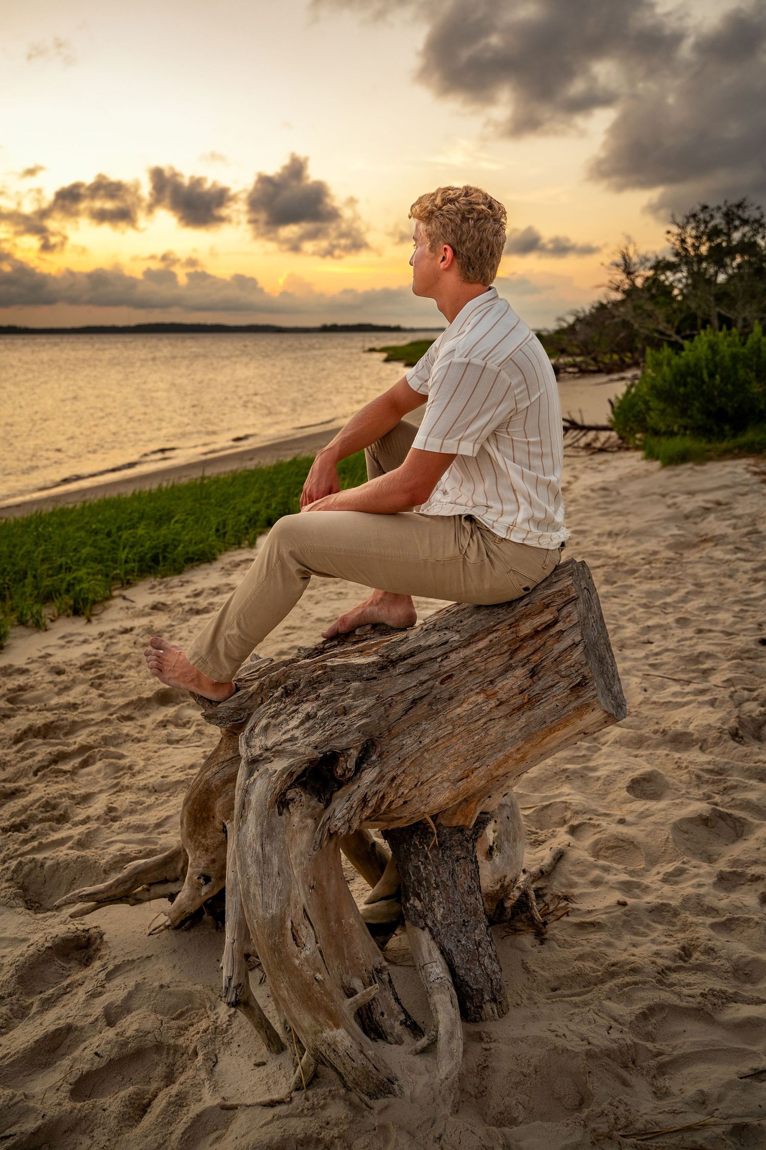 Peaceful sunset scene of person sitting on driftwood at beach during golden hour.